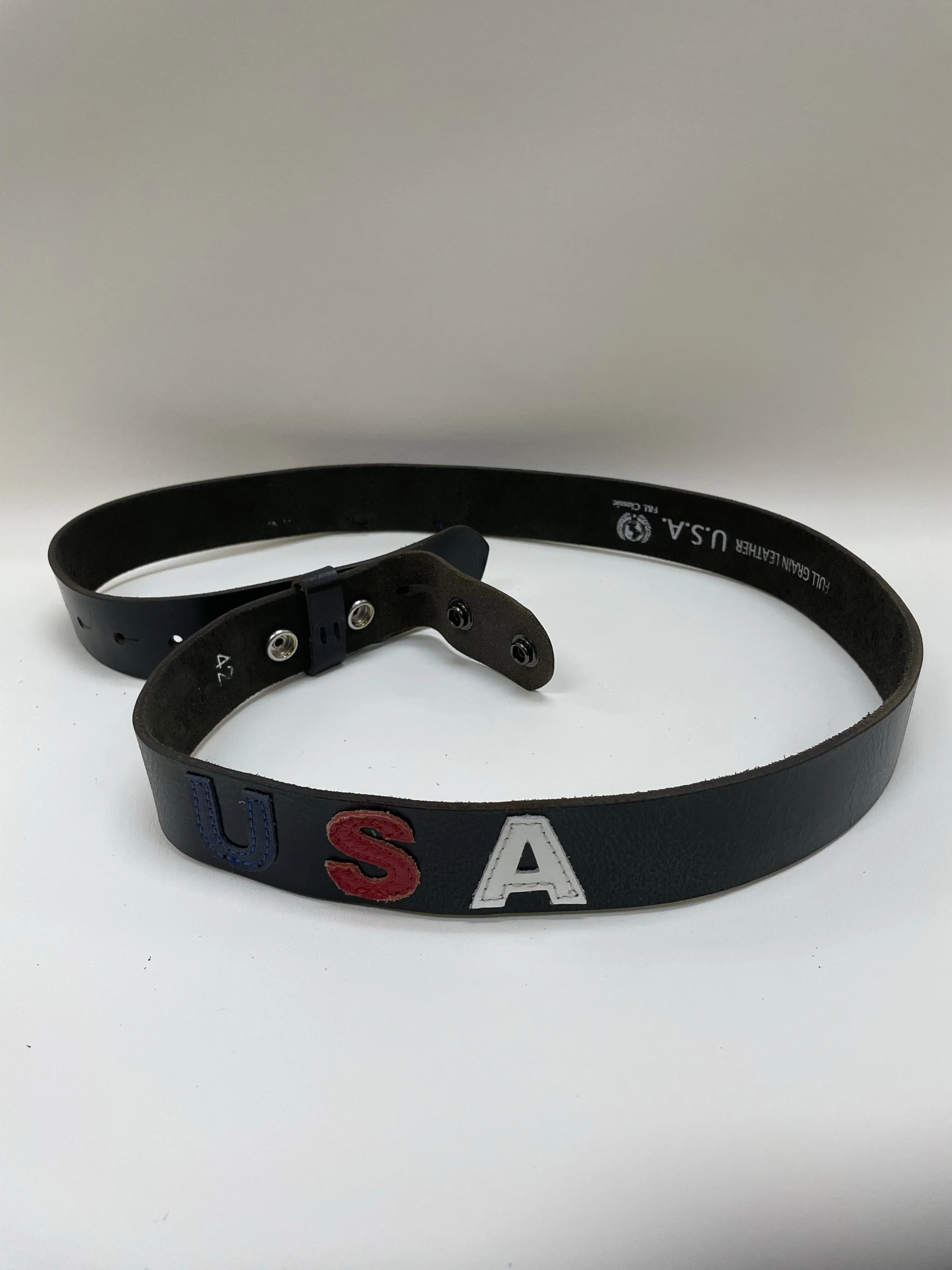 A black leather belt with embroidered letters spelling "USA" in blue, red, and white, lying on a white surface.