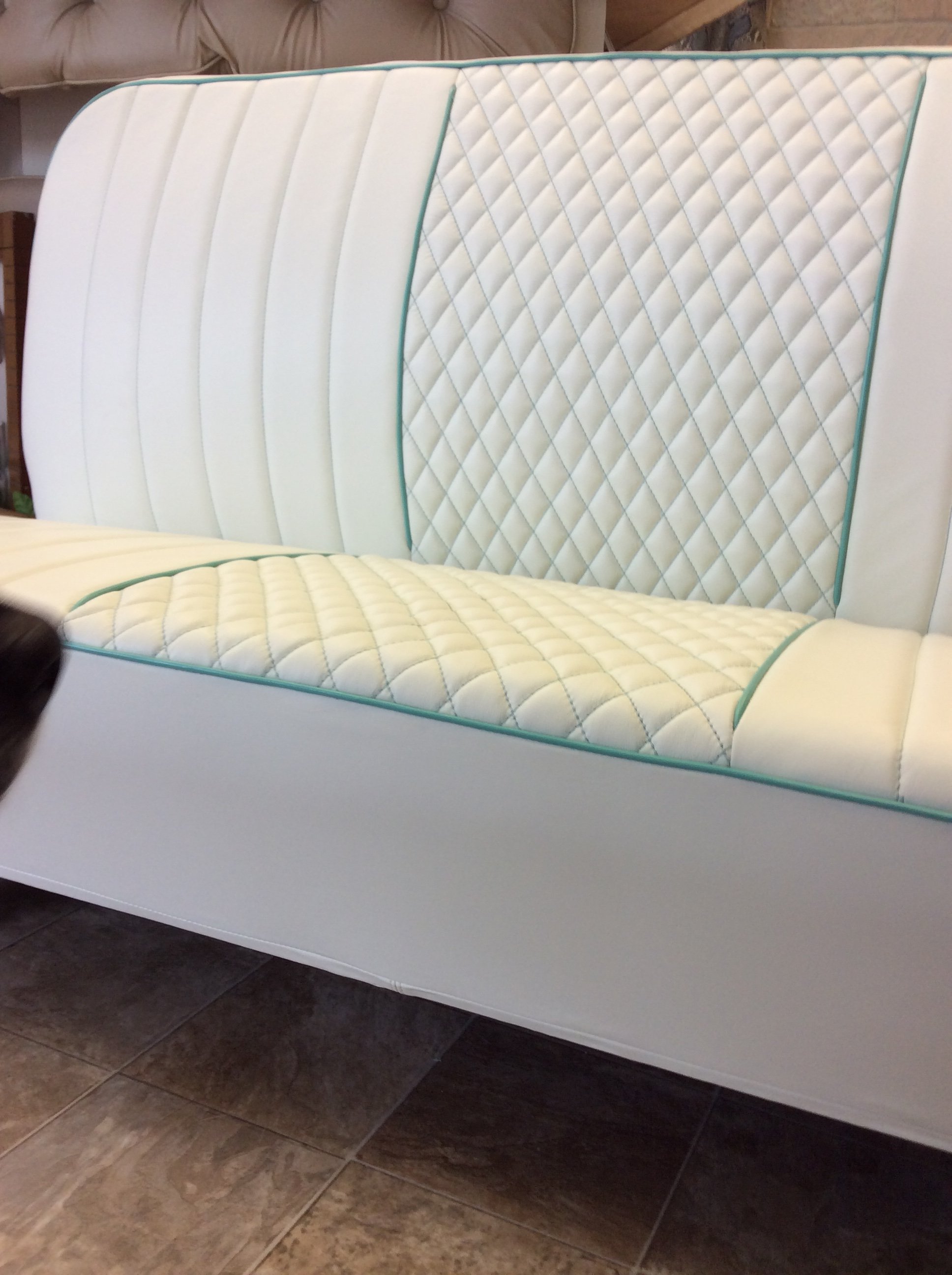 A mattress with a quilted pattern, featuring cream and teal colors, placed on the floor next to a beige sofa. The mattress is set against a tile floor.