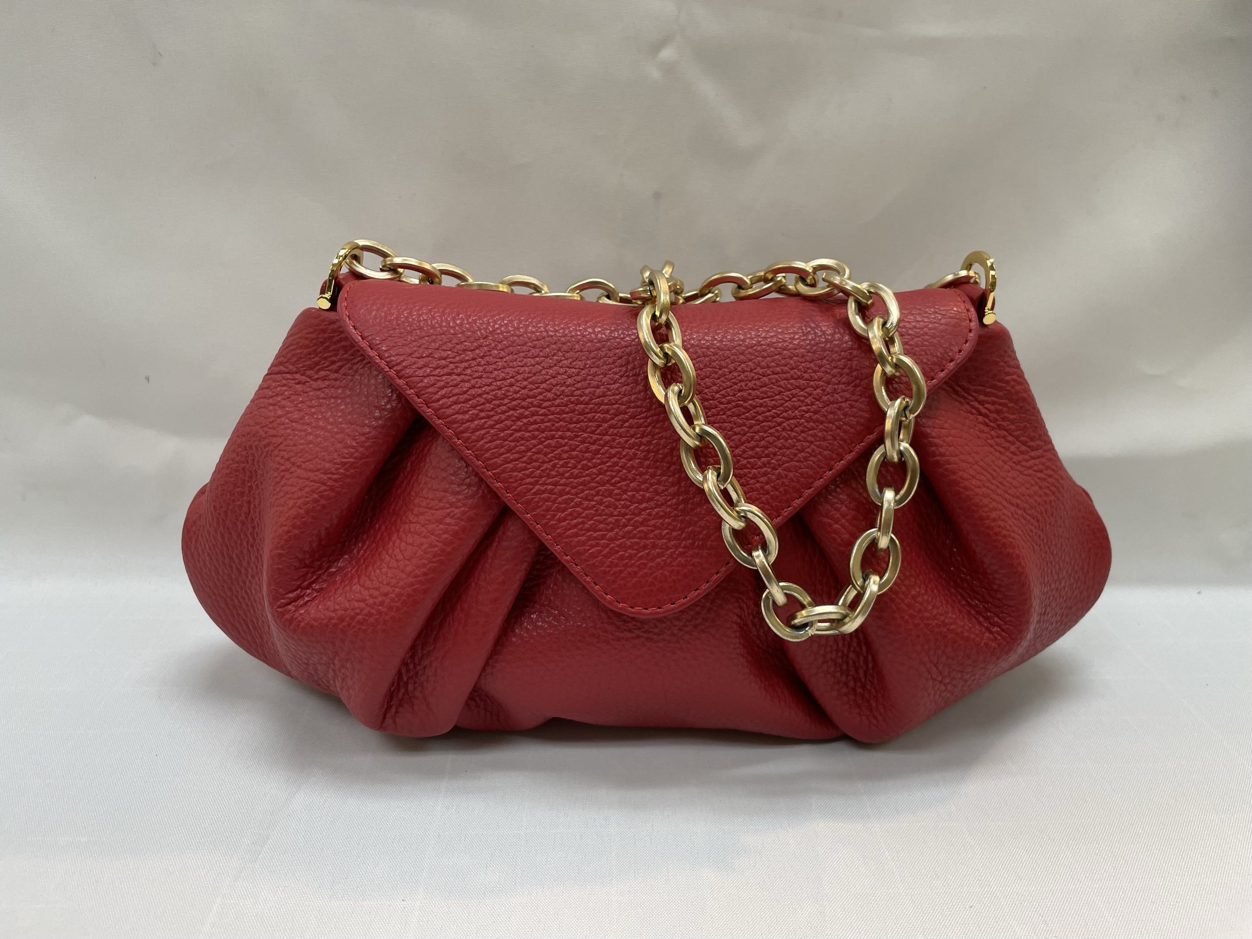A red textured leather handbag with a gold chain strap placed on a white surface with a plain background.