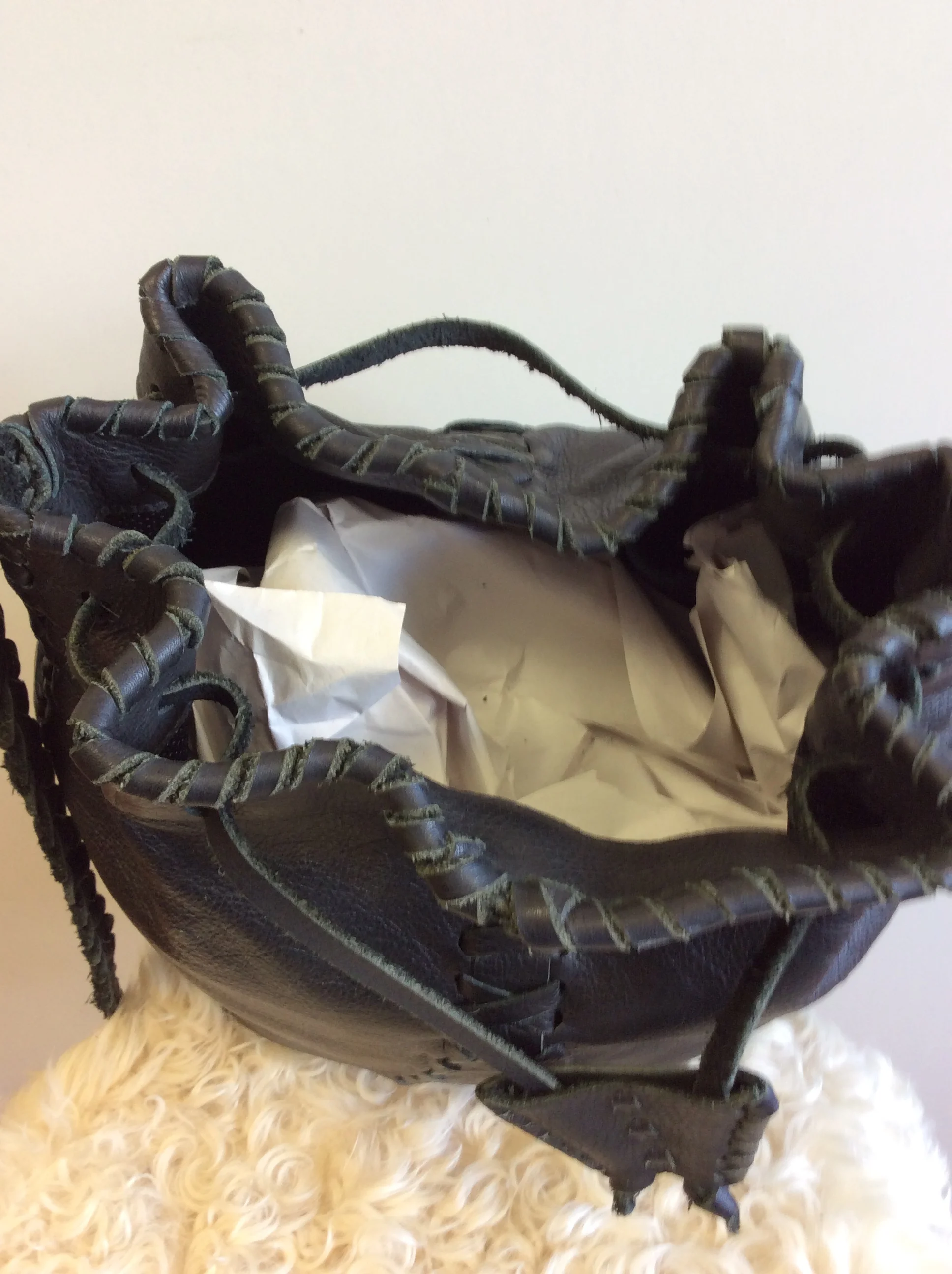 Black leather baseball glove resting on crumpled white tissue paper inside a black wire basket, on a fluffy white surface.