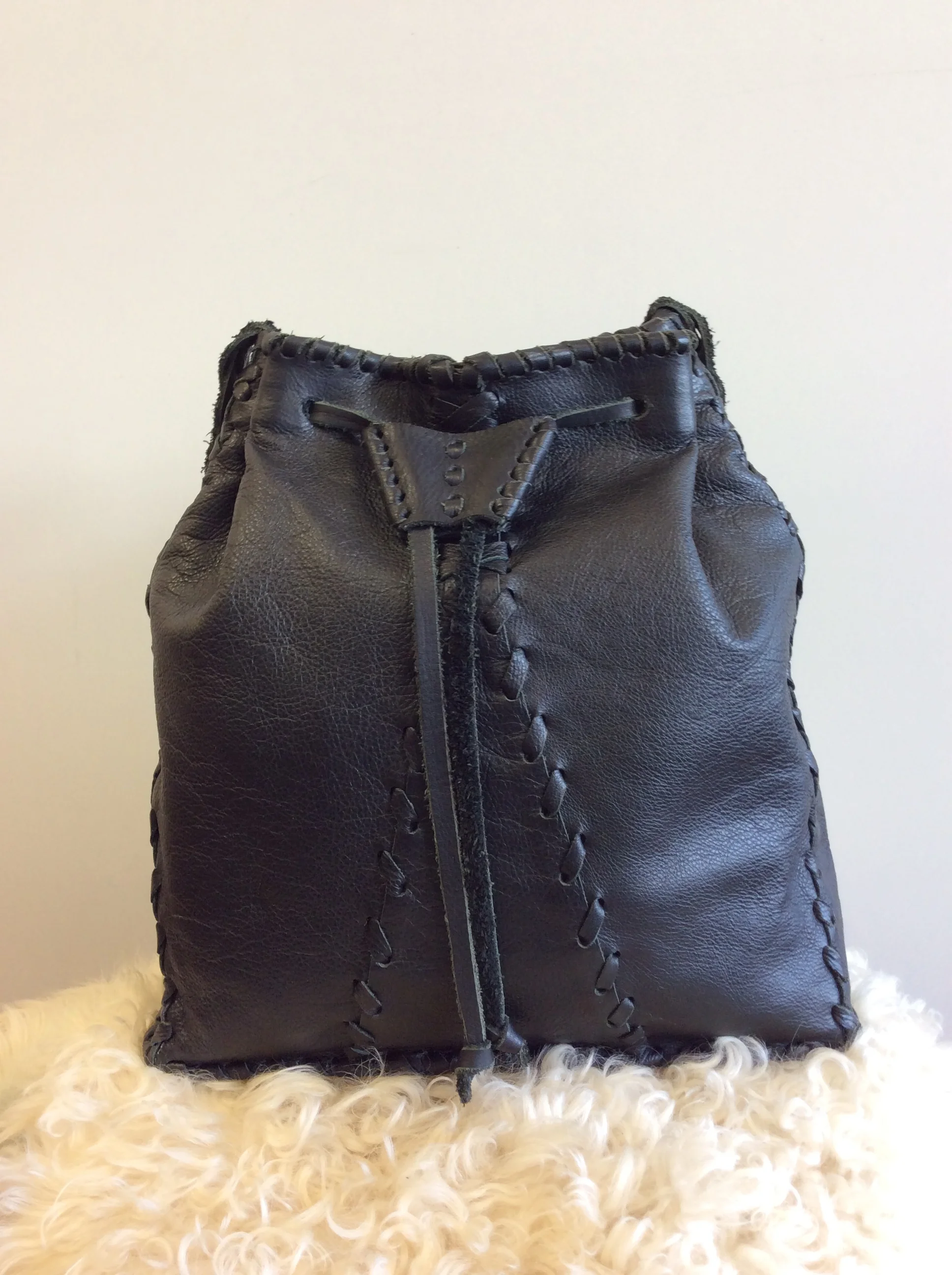 A brown leather bag with detailed stitching, placed on a fluffy white rug with a plain white wall in the background.