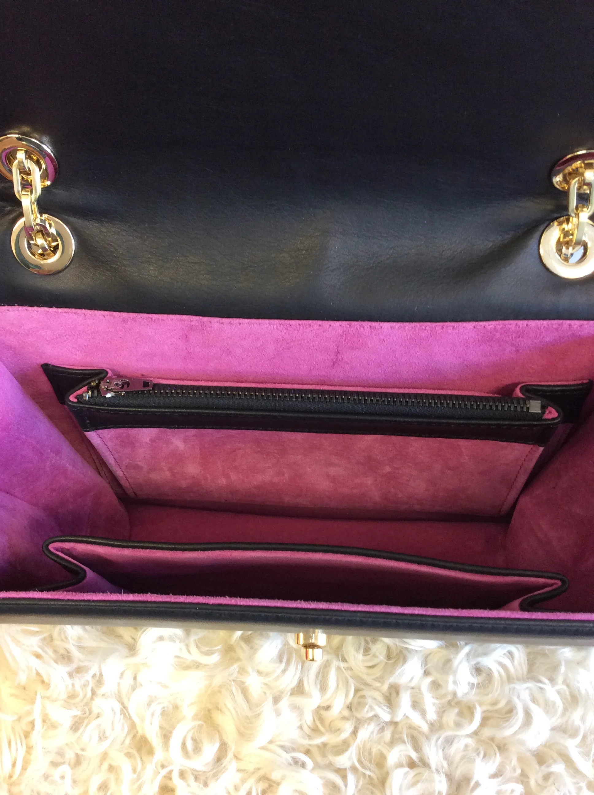 Inside view of a pink and black handbag with a zippered pocket, showing the interior lined with pink fabric, and gold metal chain details on the exterior.