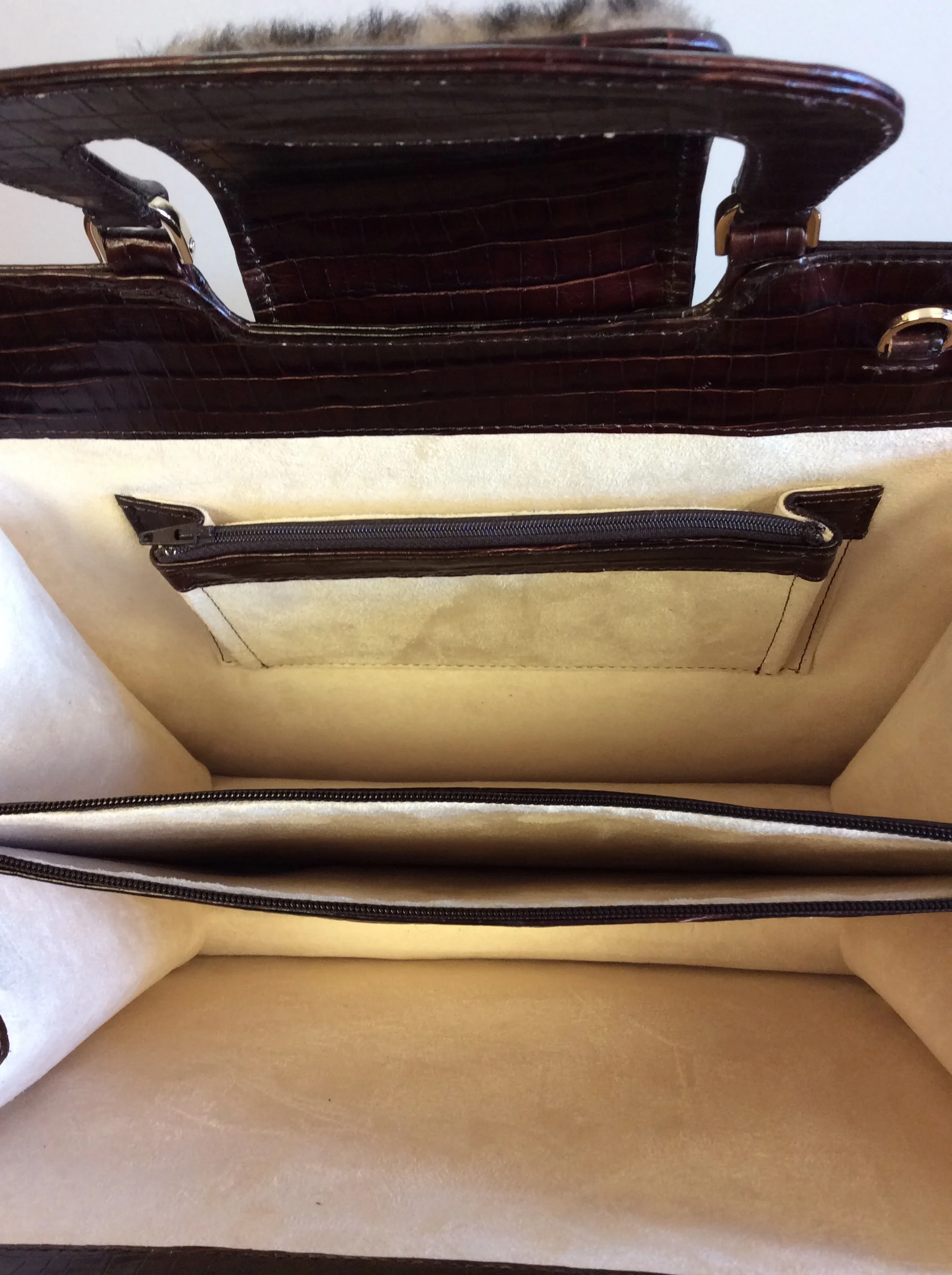The image shows the inside of a beige-colored bag or suitcase with multiple compartments and zippers. The compartments have dark brown and cream-colored finishes with a crocodile skin pattern on some of the material.