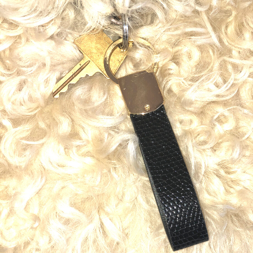 Keychain with a scented black leather strap and keys, resting on a fluffy white fabric background.