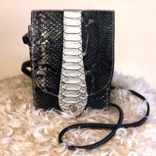 A black and white purse with a textured snake skin pattern, placed on a fluffy white surface.