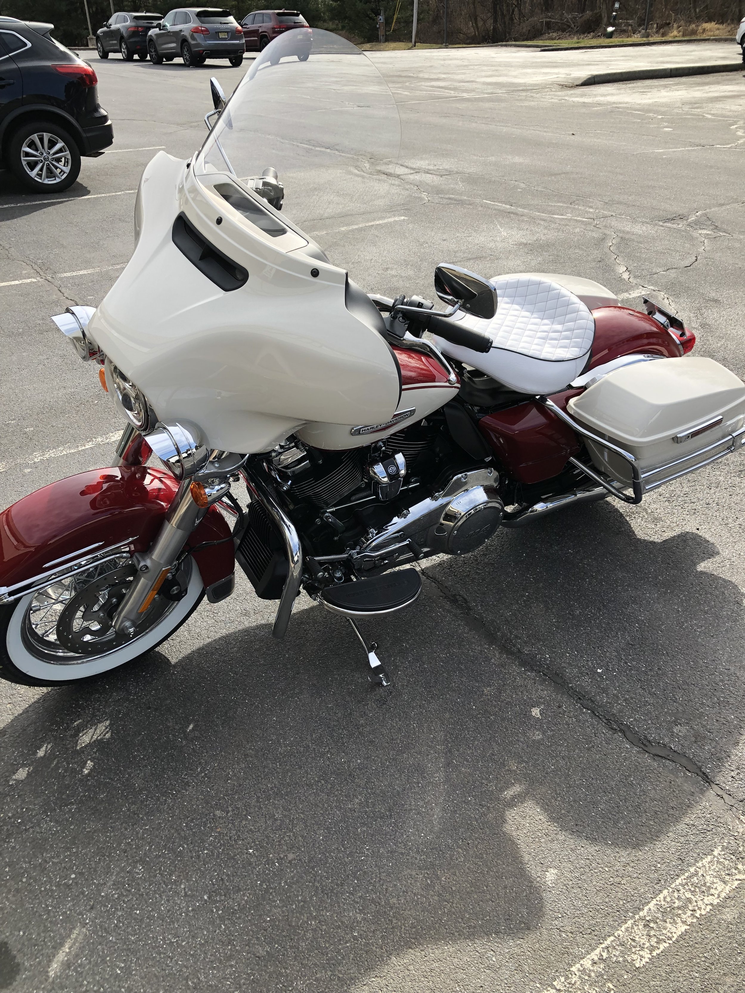A red and white Harley-Davidson touring motorcycle parked in a parking lot with several other cars around.