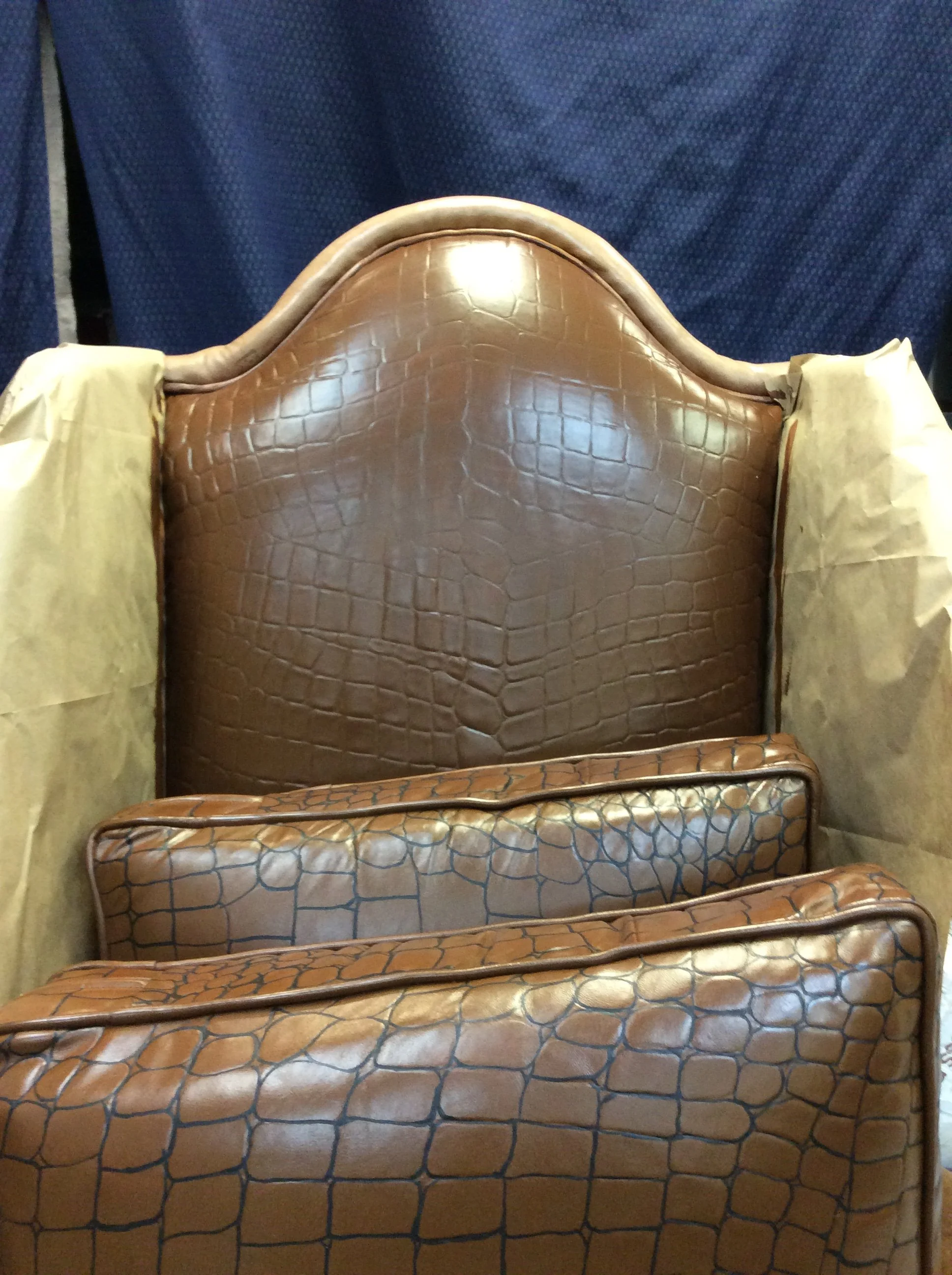 A vintage wooden headboard with a curved top, brown faux crocodile leather upholstery, and a matching footboard, arranged in front of a dark blue fabric background.