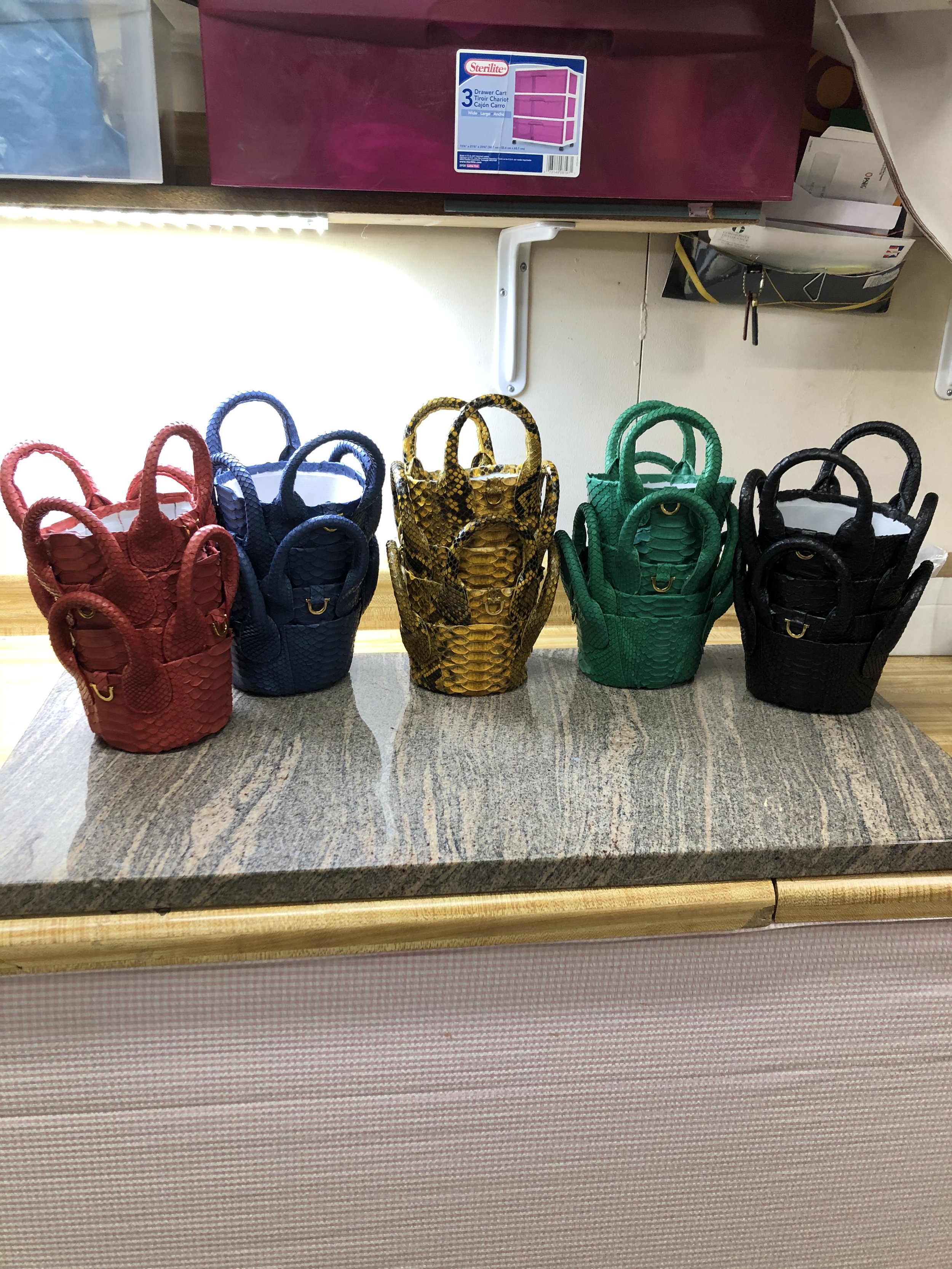 Five small handbags in red, blue, yellow, green, and black with a snake skin pattern, displayed on a granite countertop.