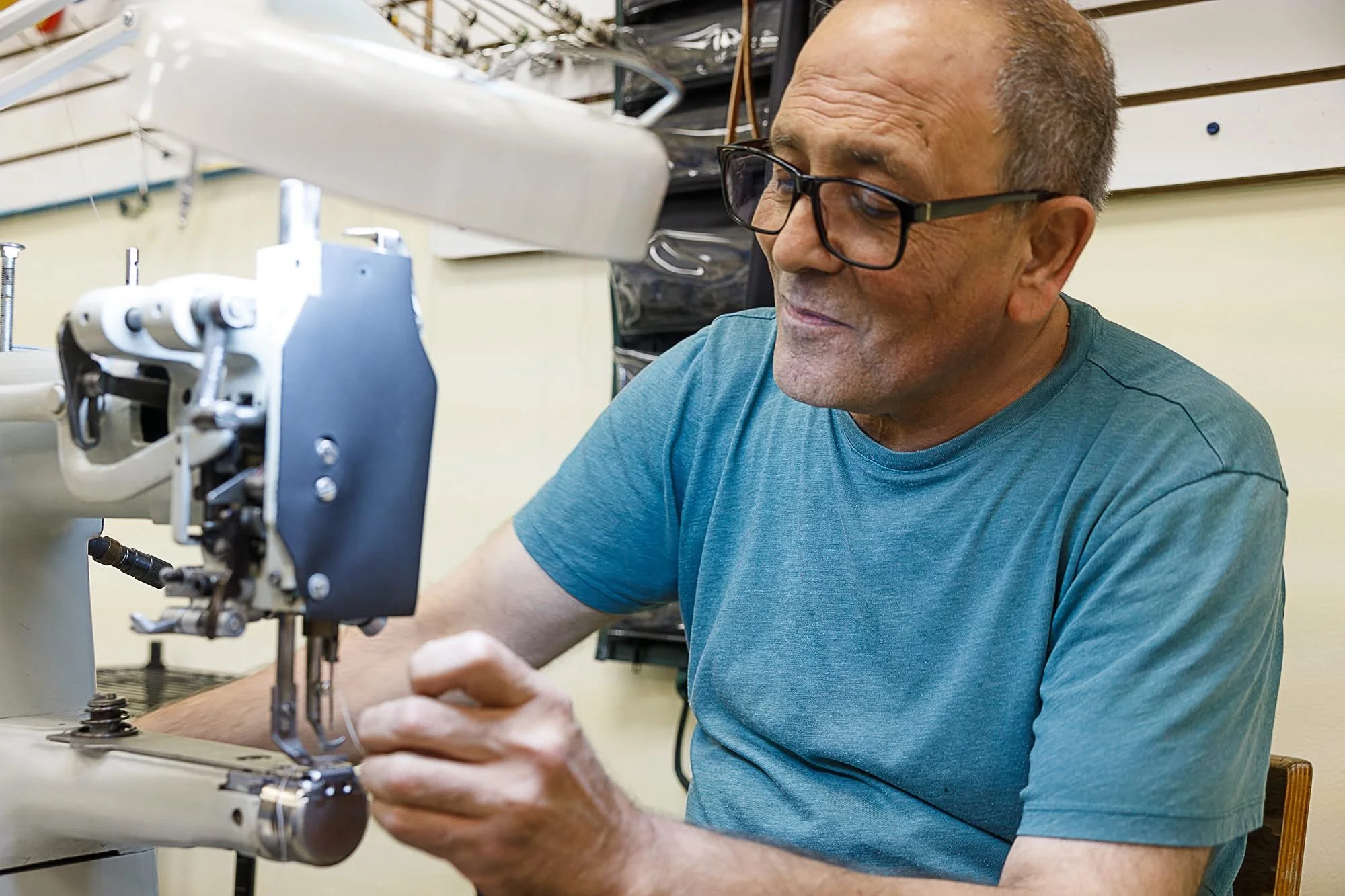 An older man with glasses working on a leather repair sewing machine.