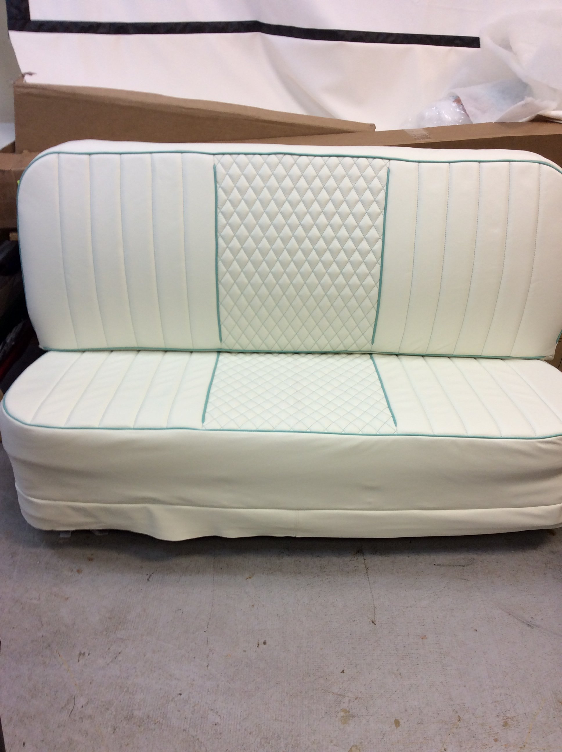 A white and teal mattress with a quilted diamond pattern on the head and foot sections, placed behind a white skirt on a concrete floor.