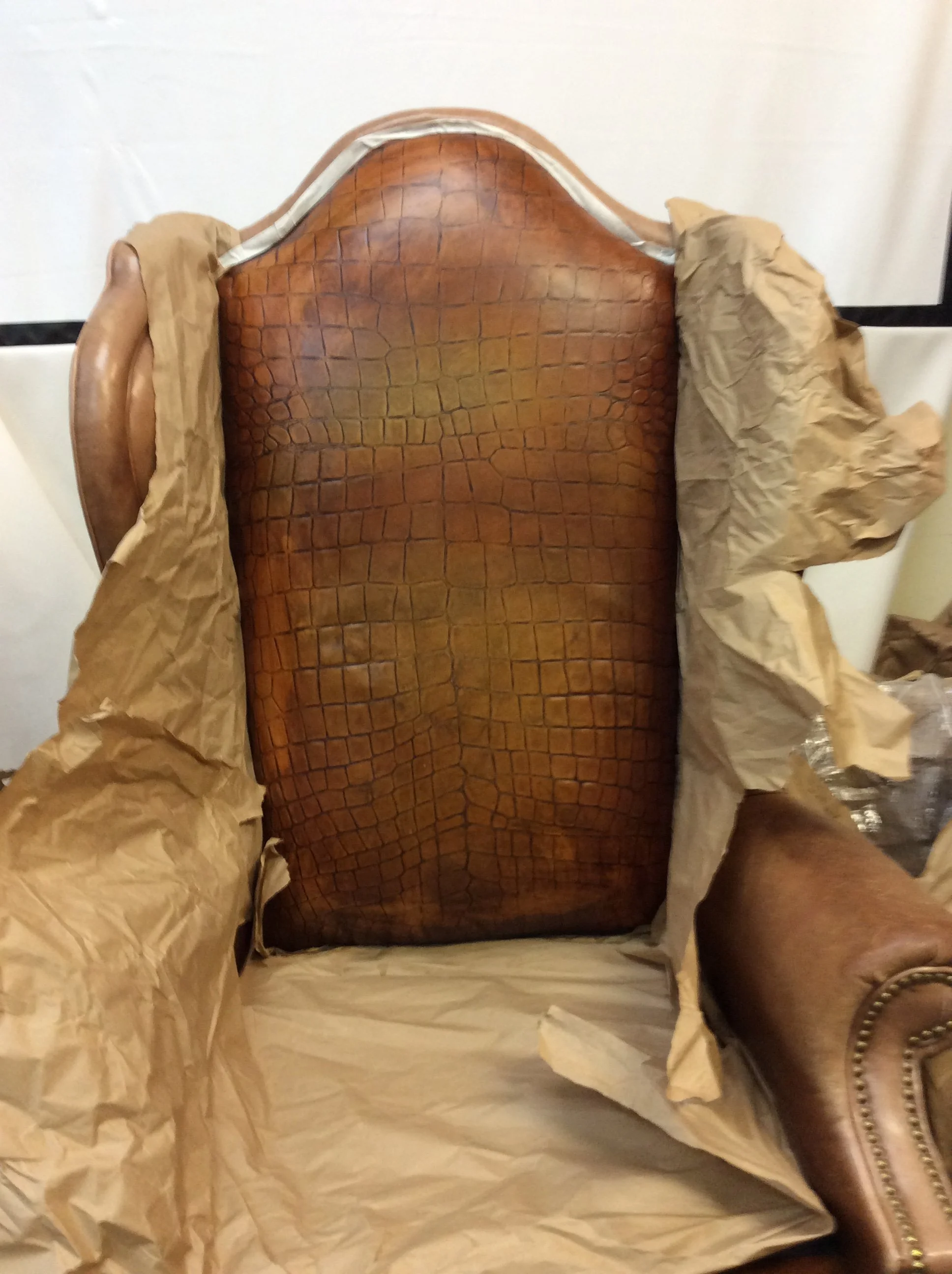 A brown leather armchair with a crocodile skin pattern, surrounded by crumpled packing paper.