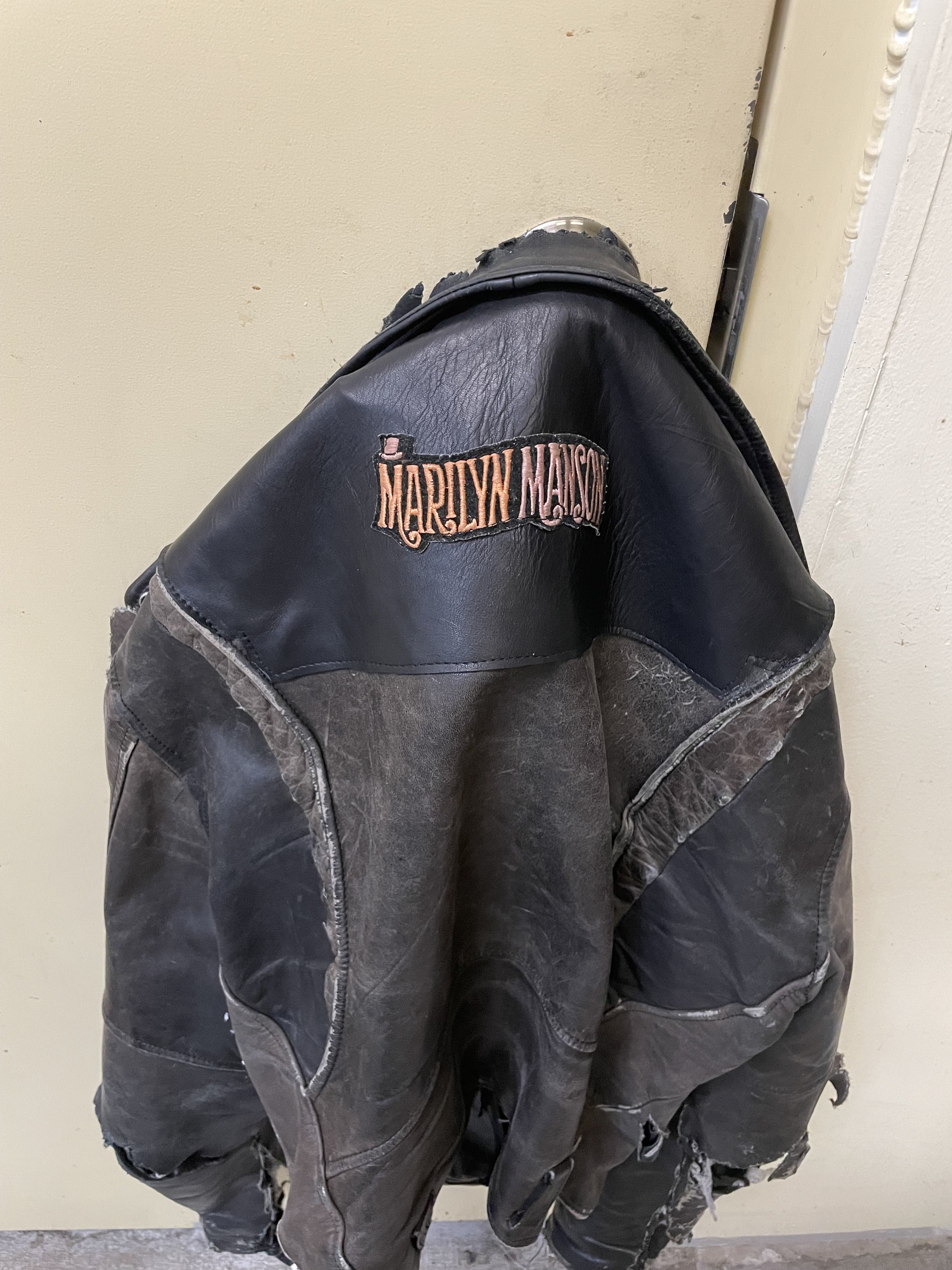 A person wearing a black and gray distressed Harley Davidson jacket sitting against a beige wall.