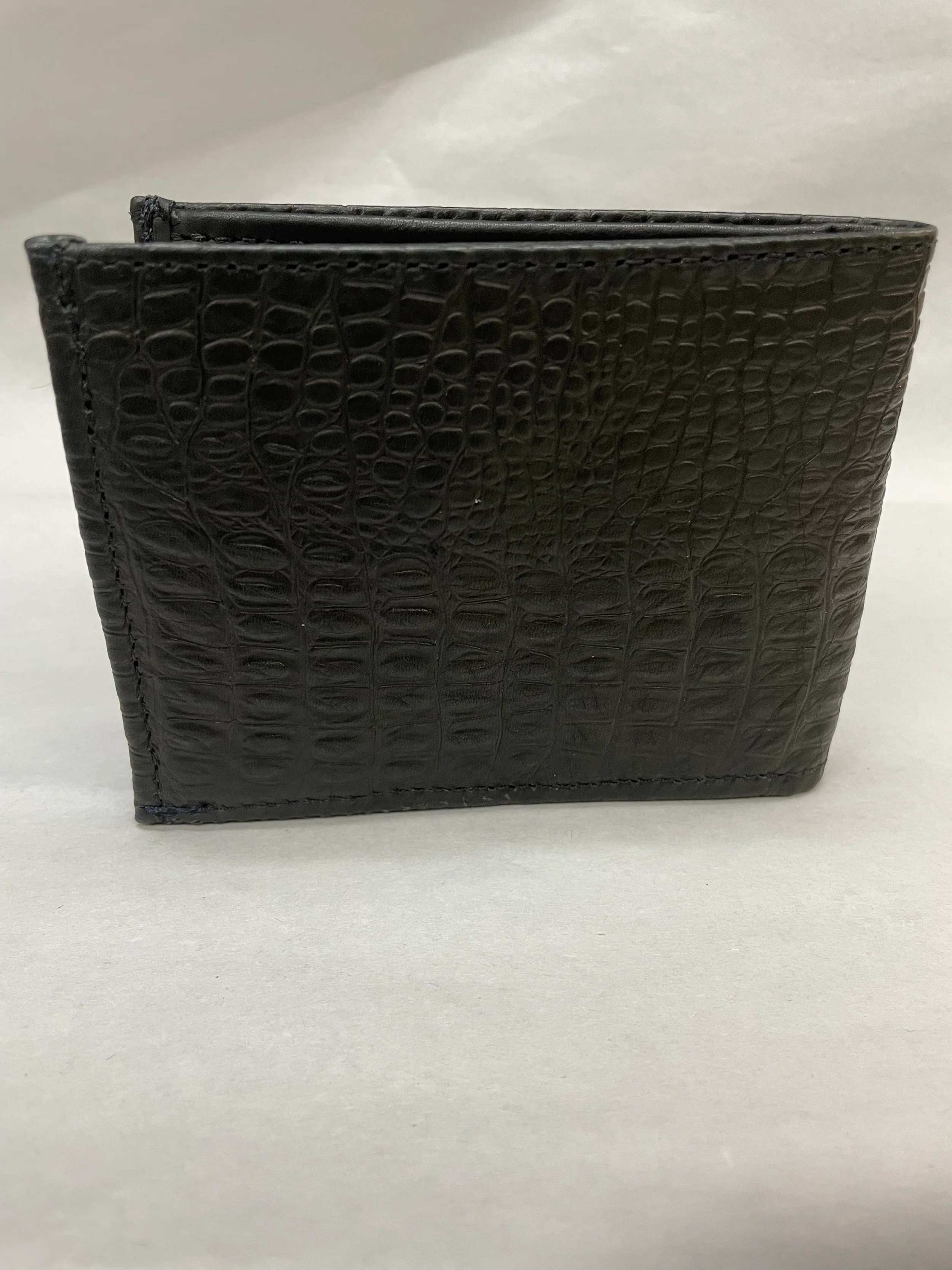 A black wallet with a textured crocodile pattern resting on a light gray surface.