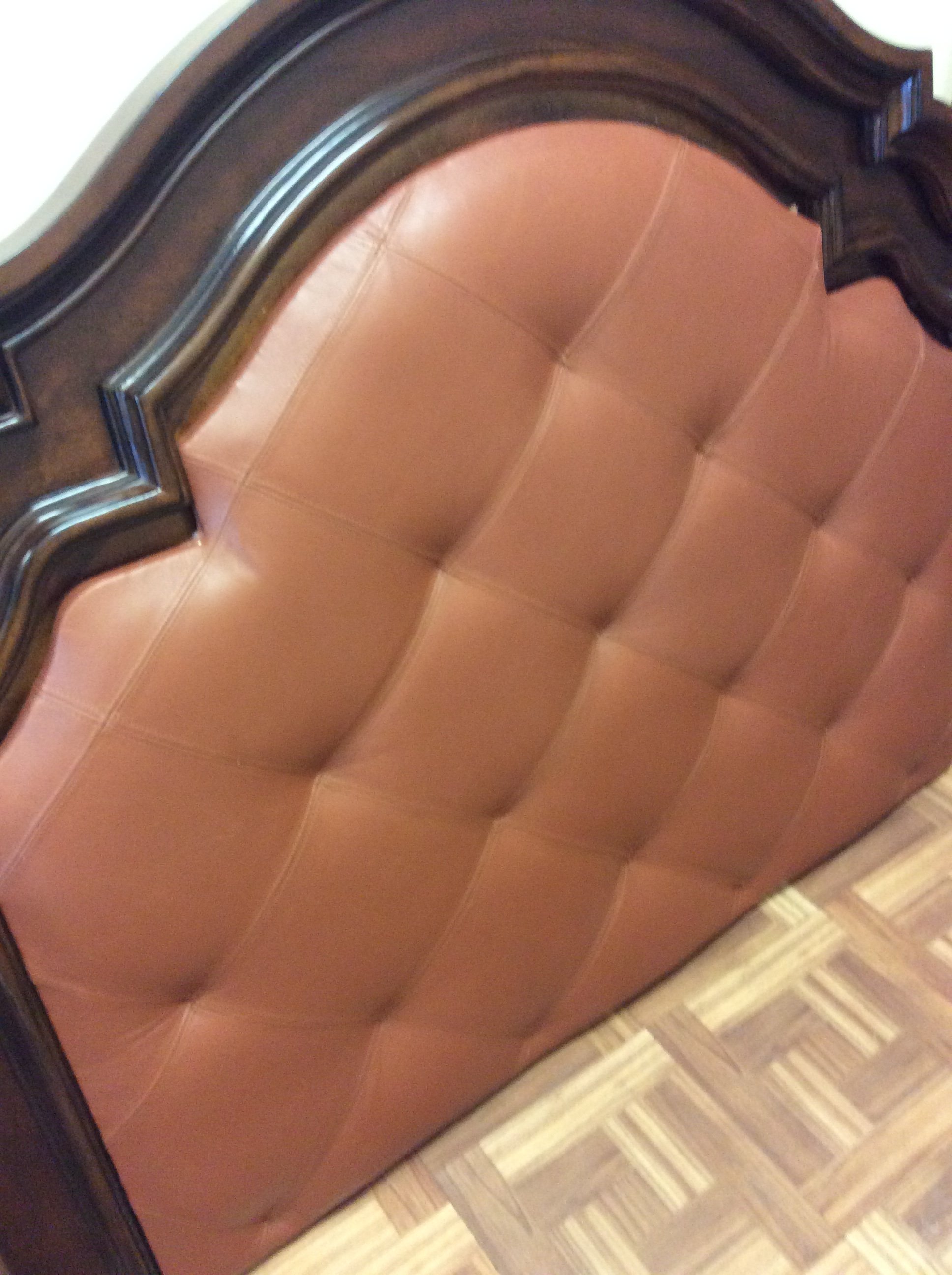Close-up photo of a wooden piece of furniture, probably a dresser or cabinet, with a brown finish and a curved top edge. The furniture is positioned next to a wood-patterned floor.