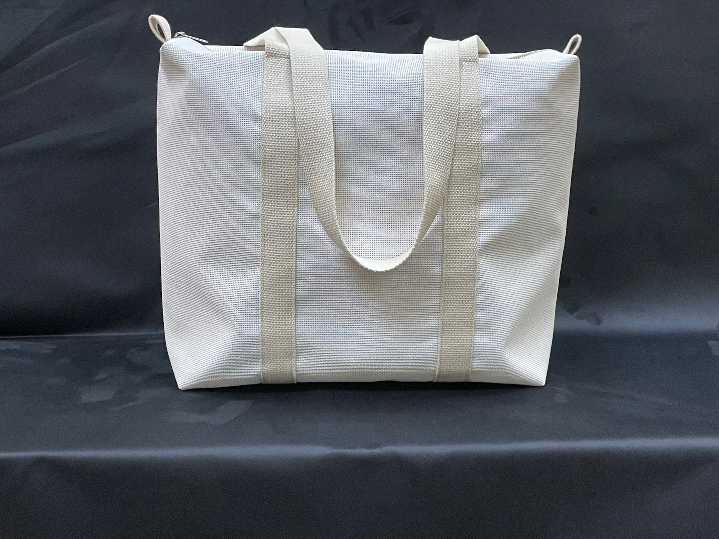 white tote bag with beige straps on a dark surface.