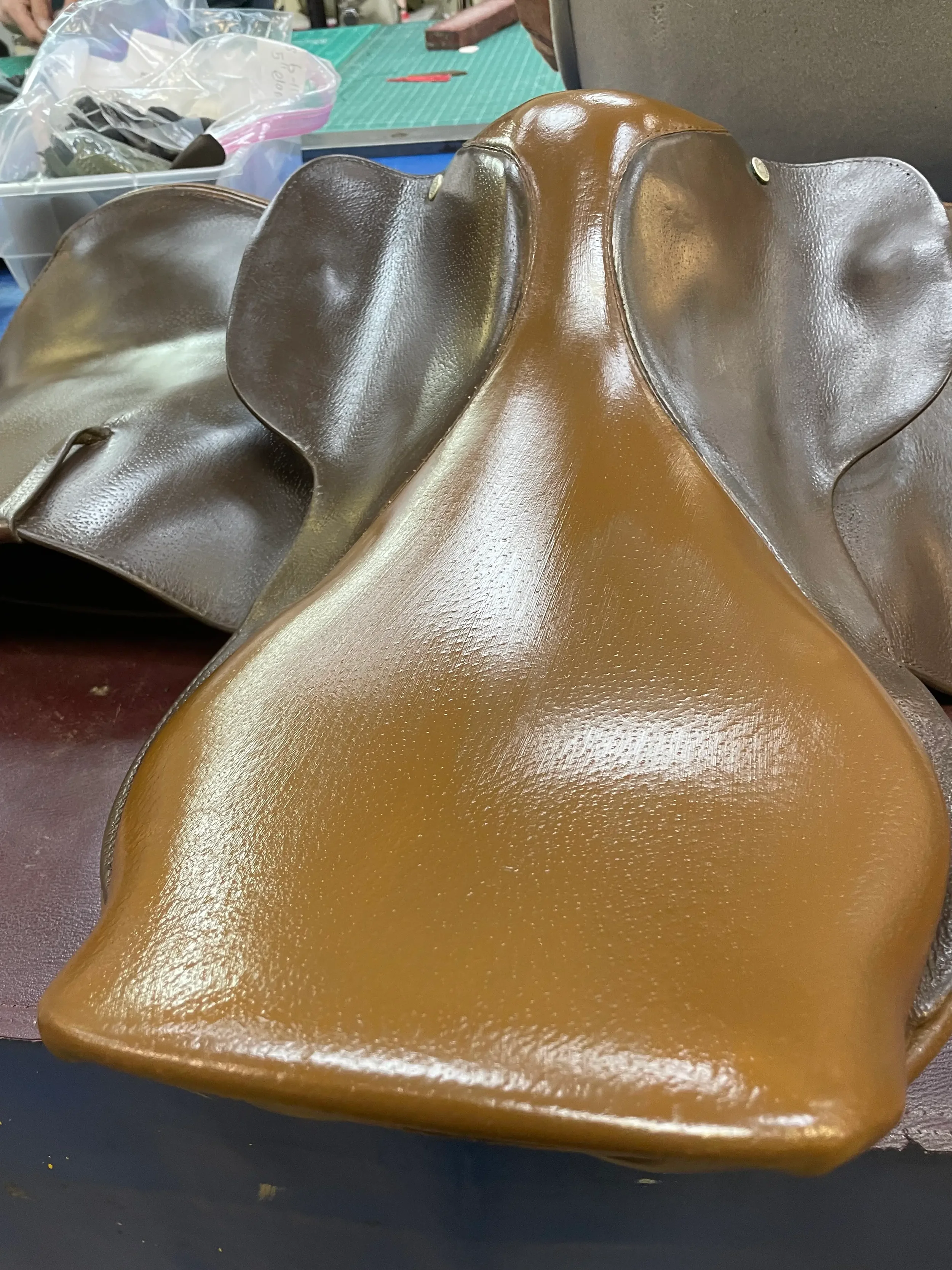 Close-up of a shiny, metallic, gold-colored mask resembling an animal face, possibly an elephant, with large ears and a smooth surface. The background shows a workspace with a green cutting mat, plastic bags, and other tools.