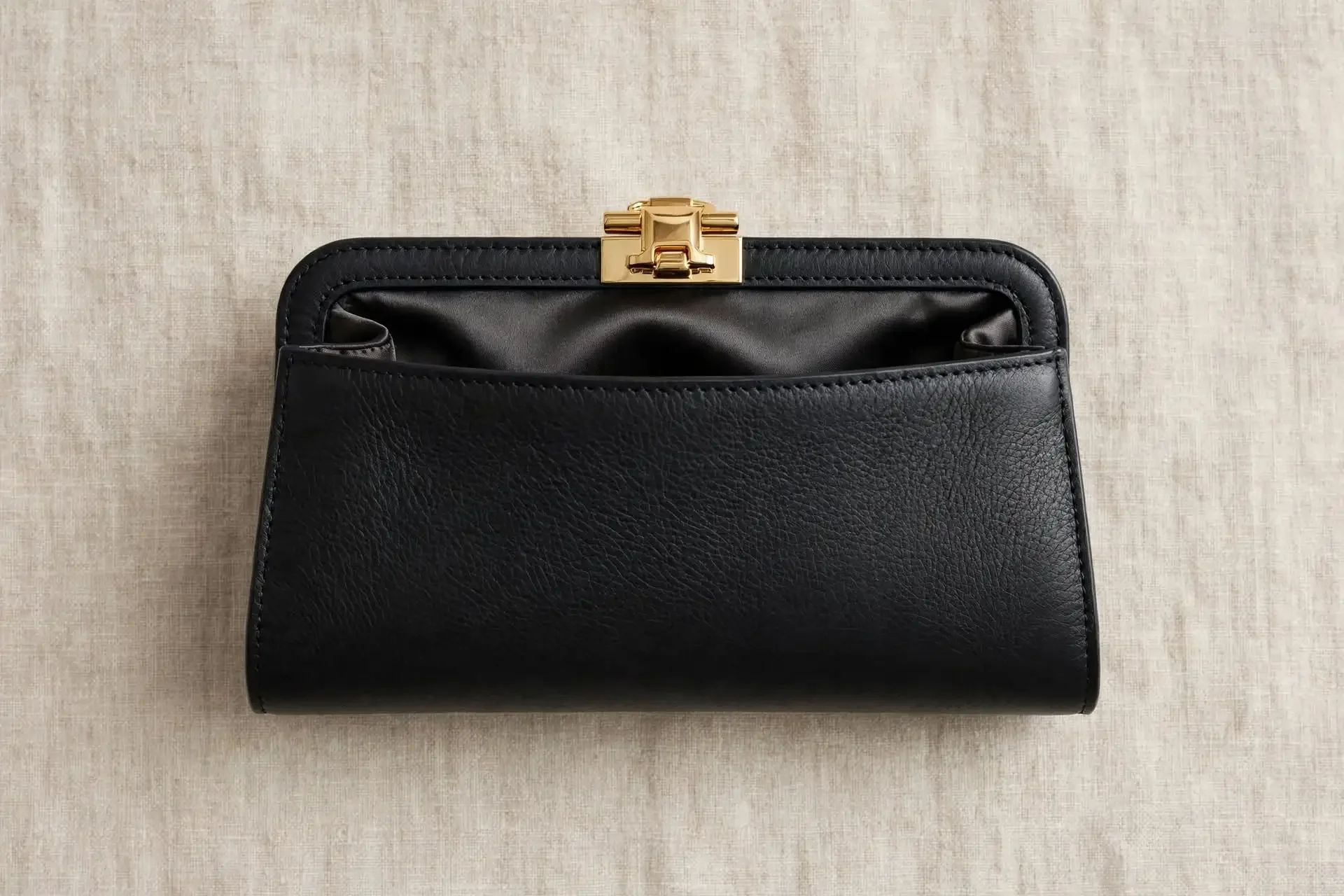 A black leather purse with a gold clasp on a beige textured surface.