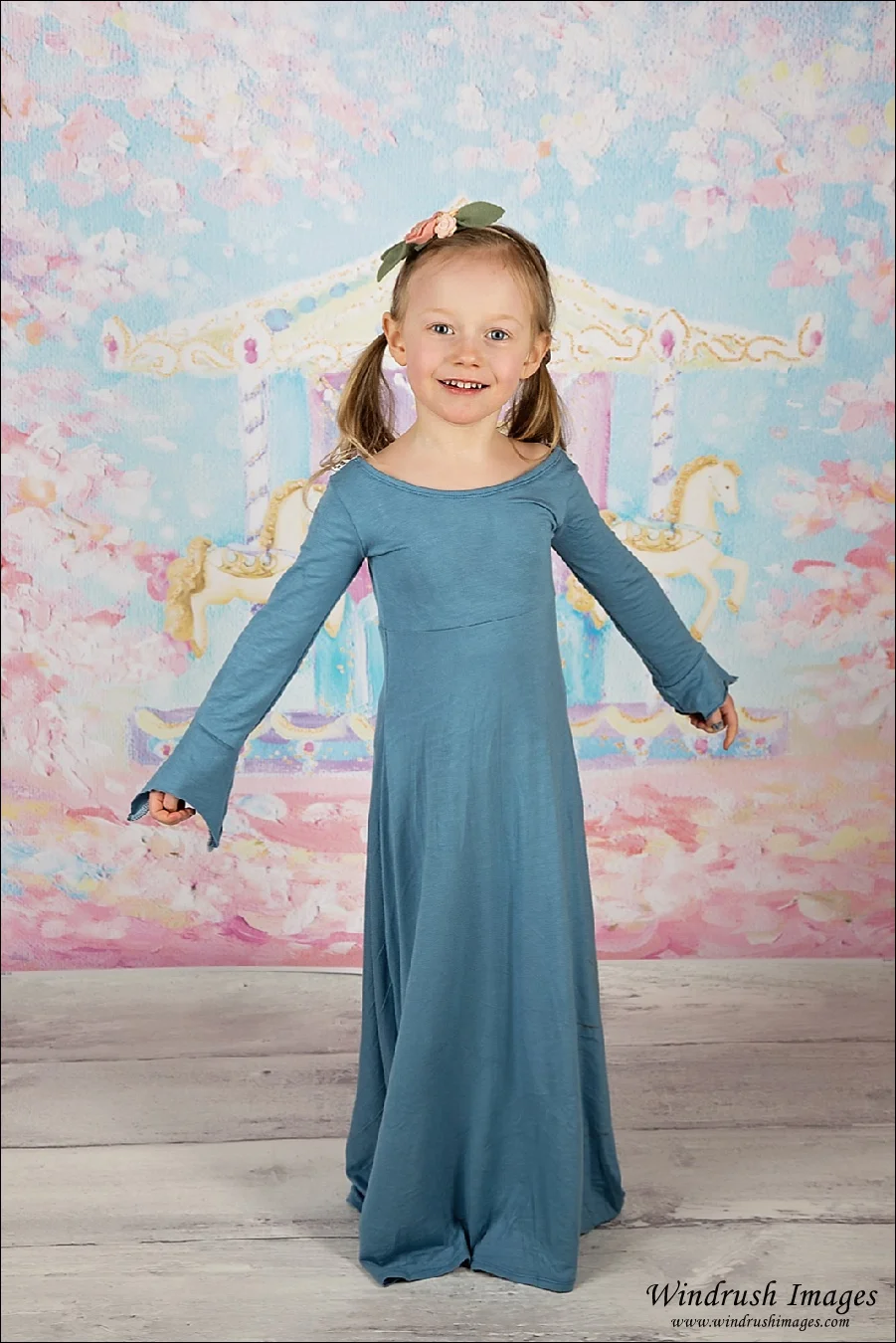 Little girl twirling in blue dress with carousel background for spring mini pictures in Calgary studio
