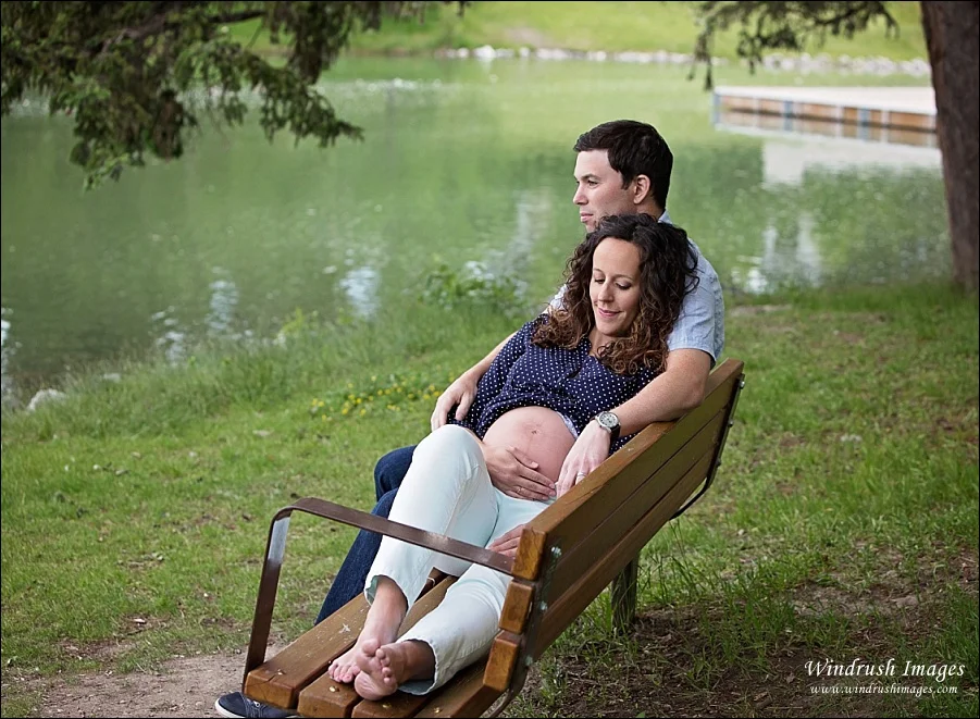 Maternity-photos-in-Calgary-of-lovely-couple-relaxing-on-a-bench-at-Bowness-Park-lagoon.jpg