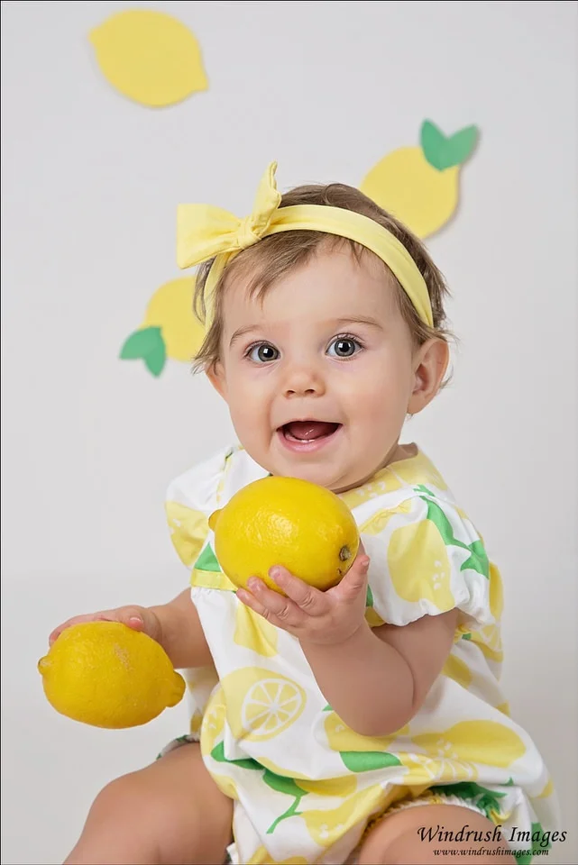 adorable-one-year-old-girl-holding-lemons-at-the-beginning-of-a-lemon-themed-cake-smash-photography-session-in-north-west-Calgary