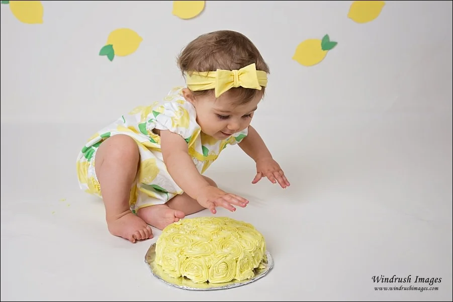 Little-girl-starting-to-smash-yellow-cake-in-lemon-cake-smash-photo-shoot-in-Arbour-Lake-Calgary