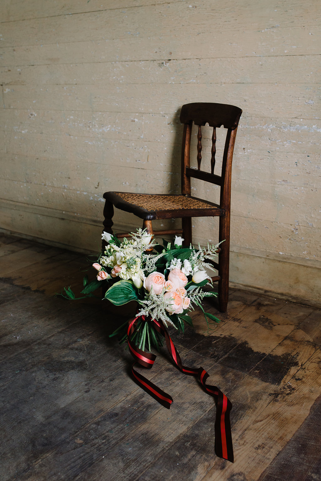 Bouquet with hosta, astilbe, garden roses, stock, tulip, campanula and pea shoots resting against a 19th century cane chair. Photo by Norman Photo and Paper.