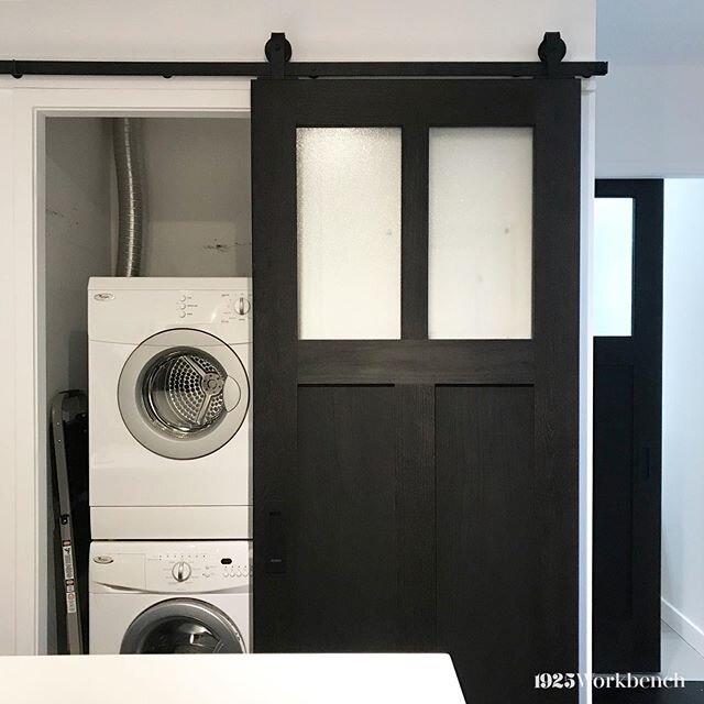 Who said you can&rsquo;t get fancy with the laundry room in your condo? Especially when it&rsquo;s across your kitchen. Our Chicago door in blackened oak on our matte black top mount hardware. We also made one for the bathroom seen here in the backgr
