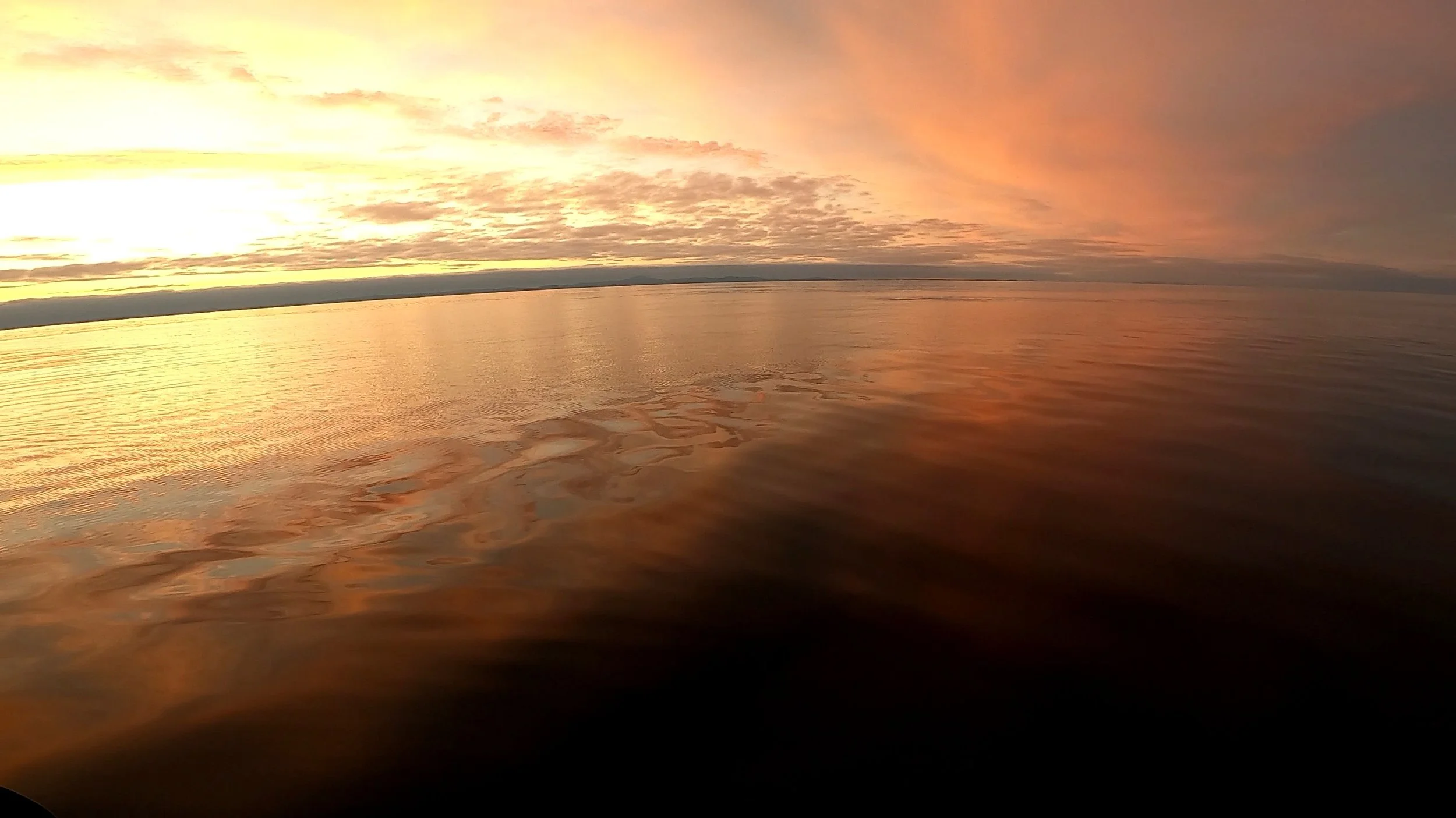 Sunset over a calm body of water with a colorful sky filled with clouds.