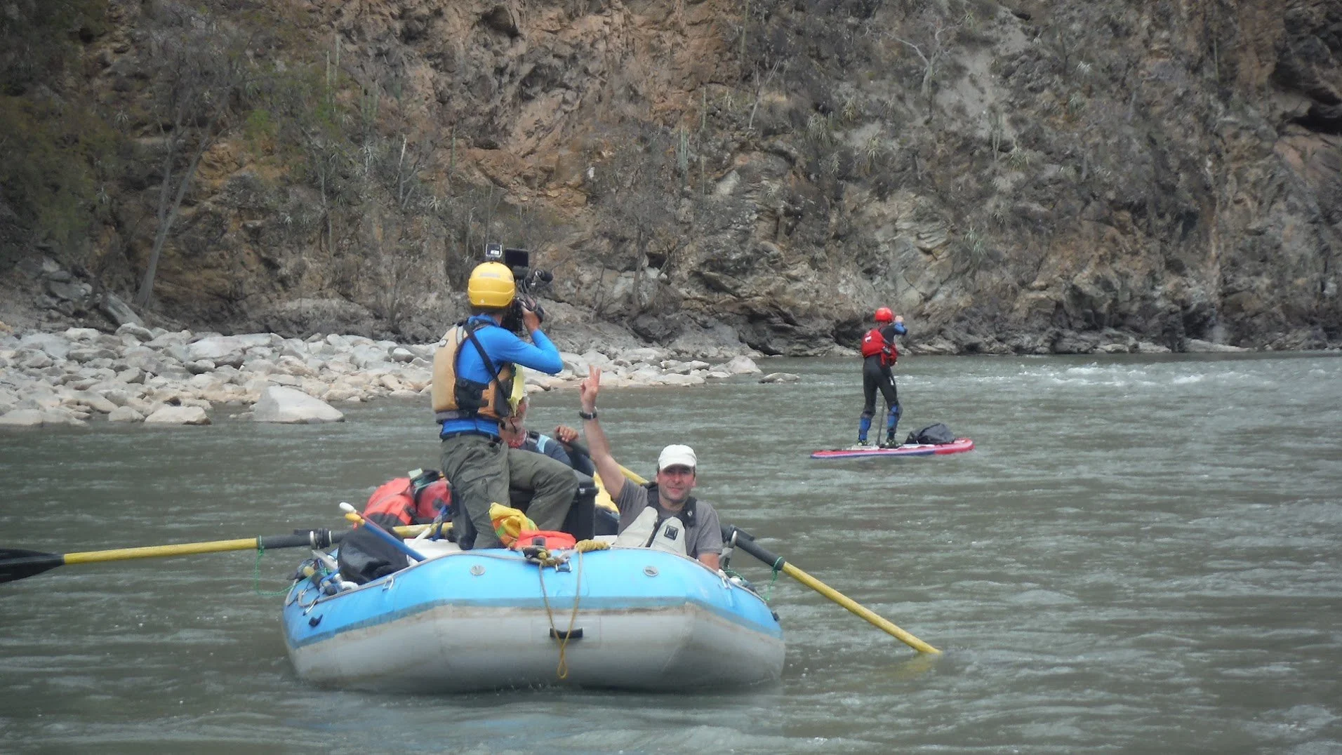 People engaging in whitewater rafting on a river surrounded by rocky and forested cliffs.