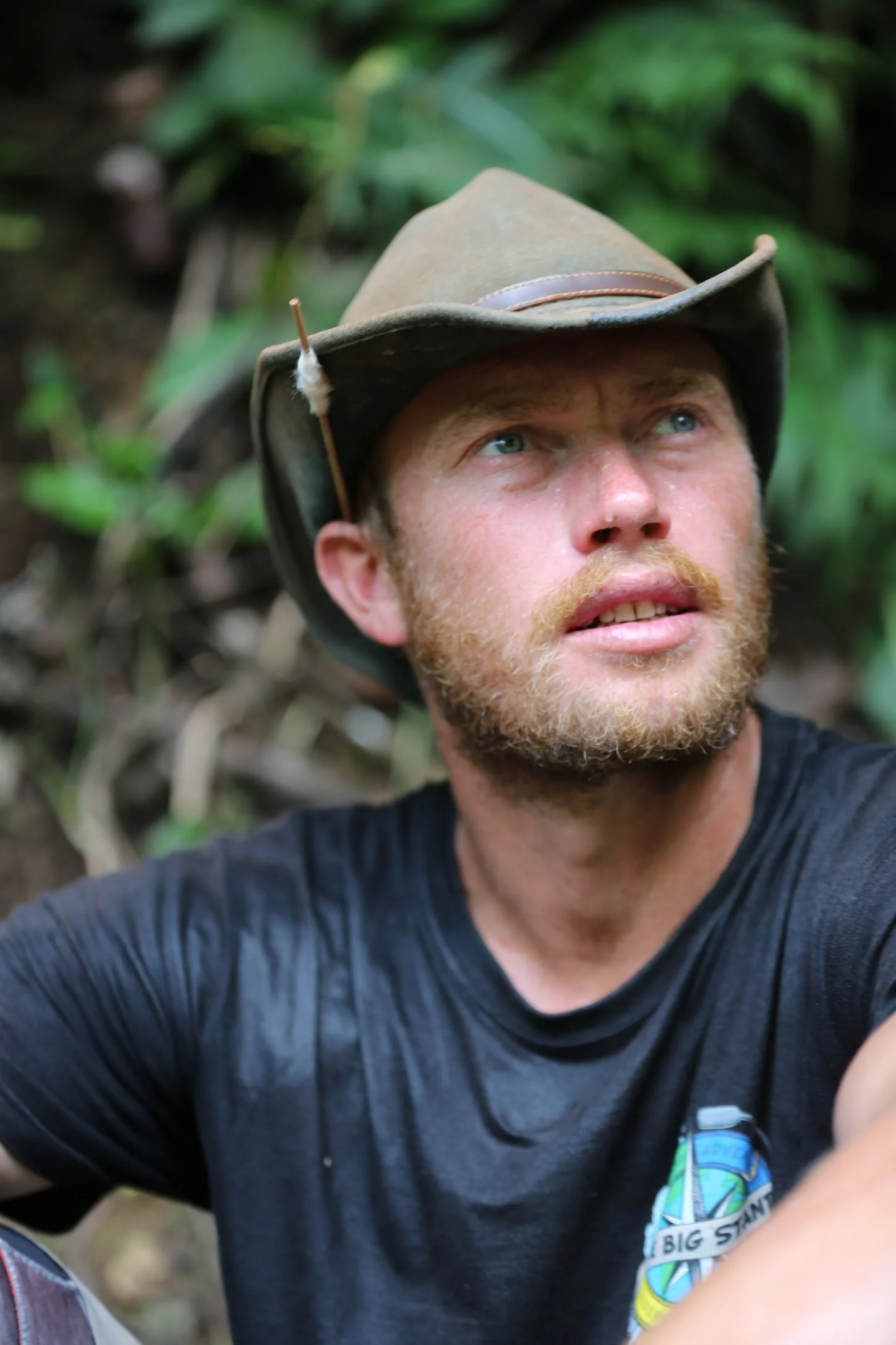 Close-up of Charlie Head wearing a wide-brimmed hat and a black t-shirt, outdoors in a Amazon jungle.