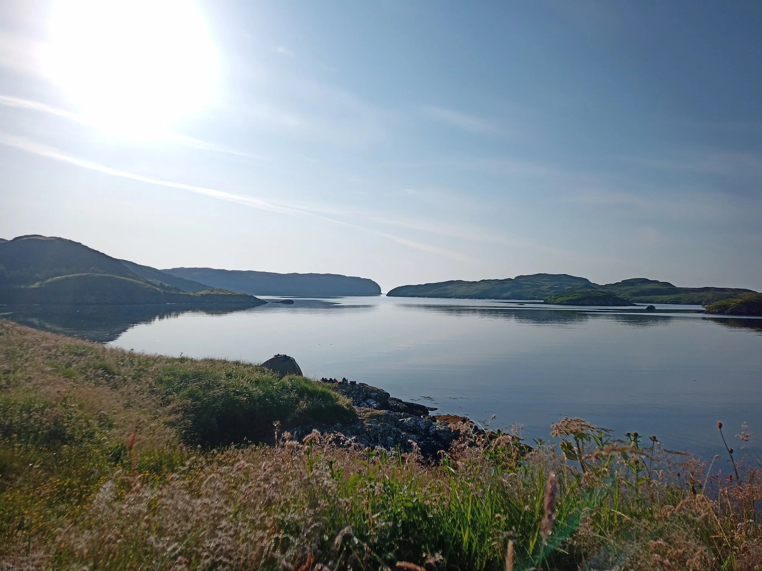 A serene lake surrounded by rolling hills under a bright blue sky.