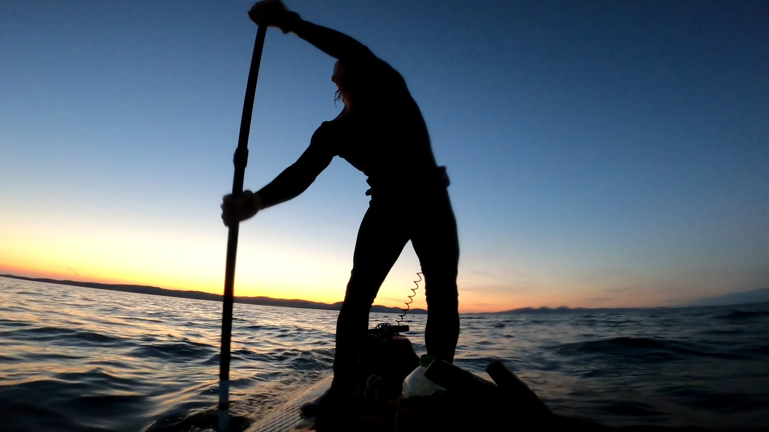 Silhouette of a person paddleboarding on a body of water during sunset.