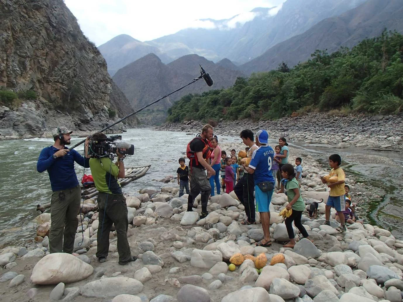 Filming crew captures scene with children by river in mountainous landscape.