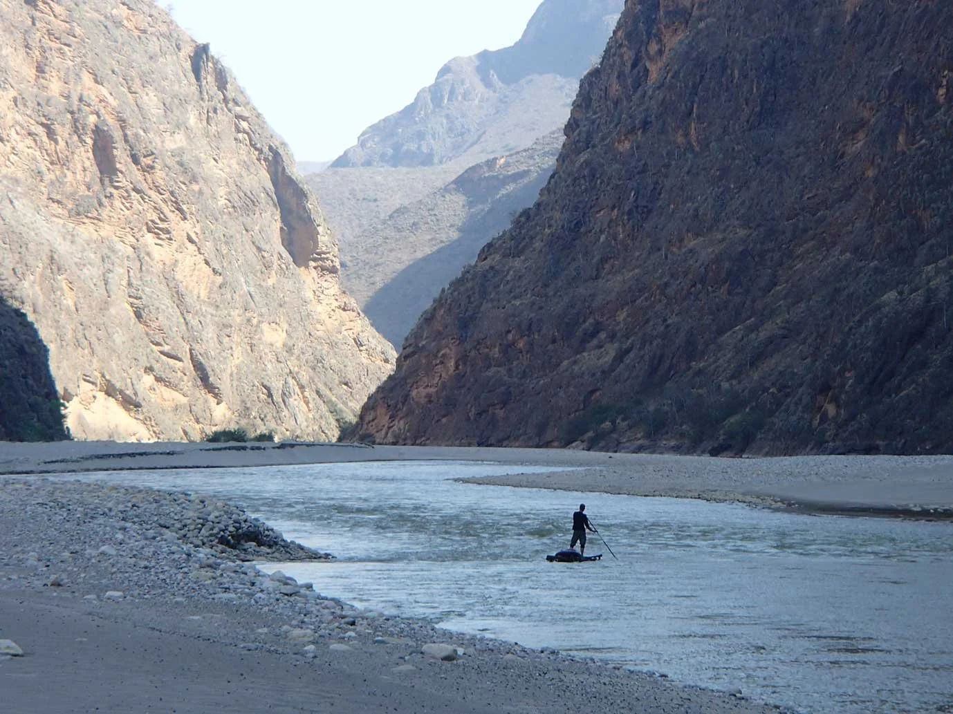 A person paddleboarding on a river surrounded by steep rocky canyon walls.