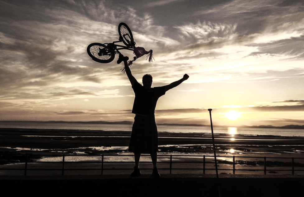 Person holding a bicycle in the air during sunset on a beach with a sunset in the background.