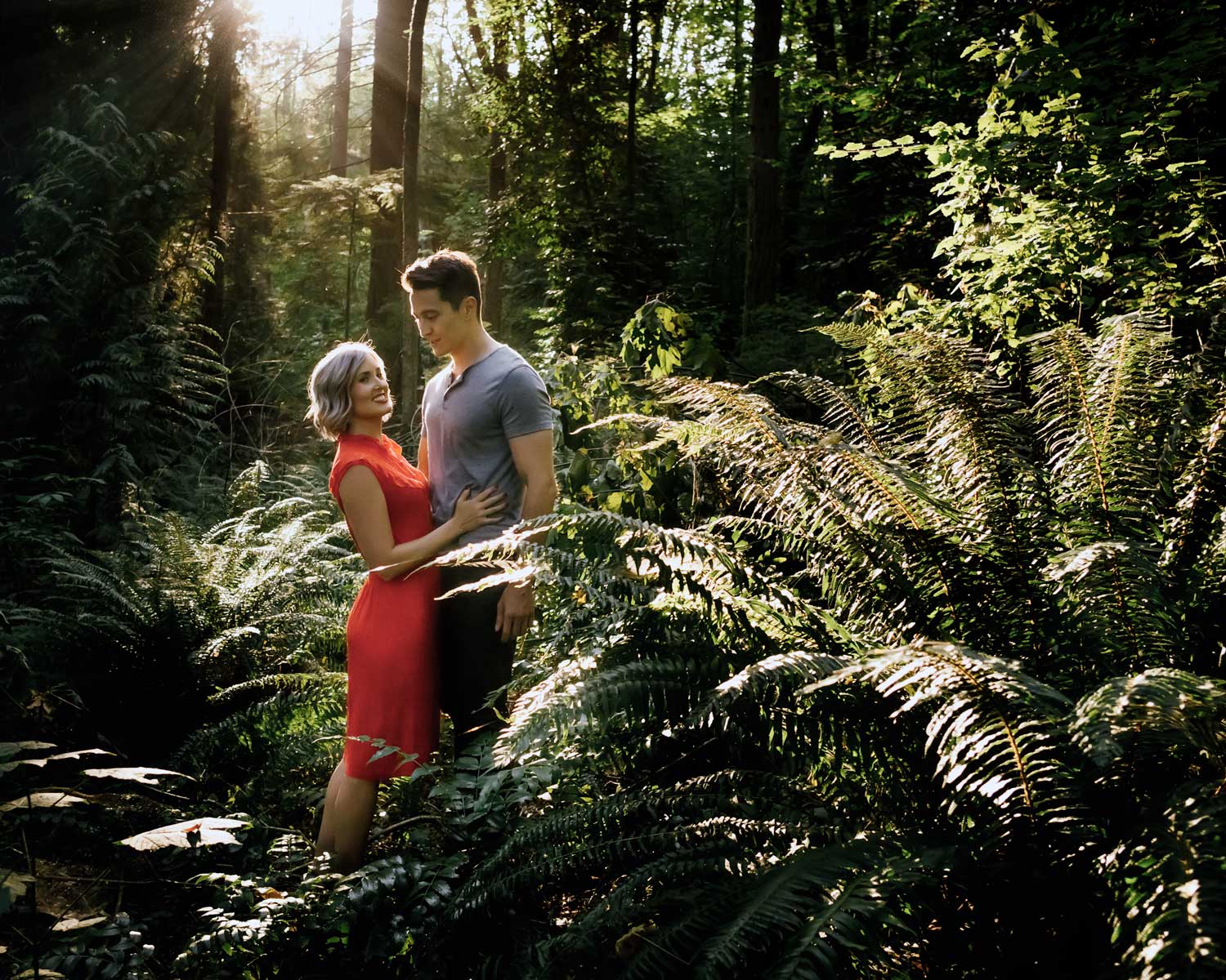 A couple kissing in a lush garden with a small waterfall, colorful bushes, and green foliage.