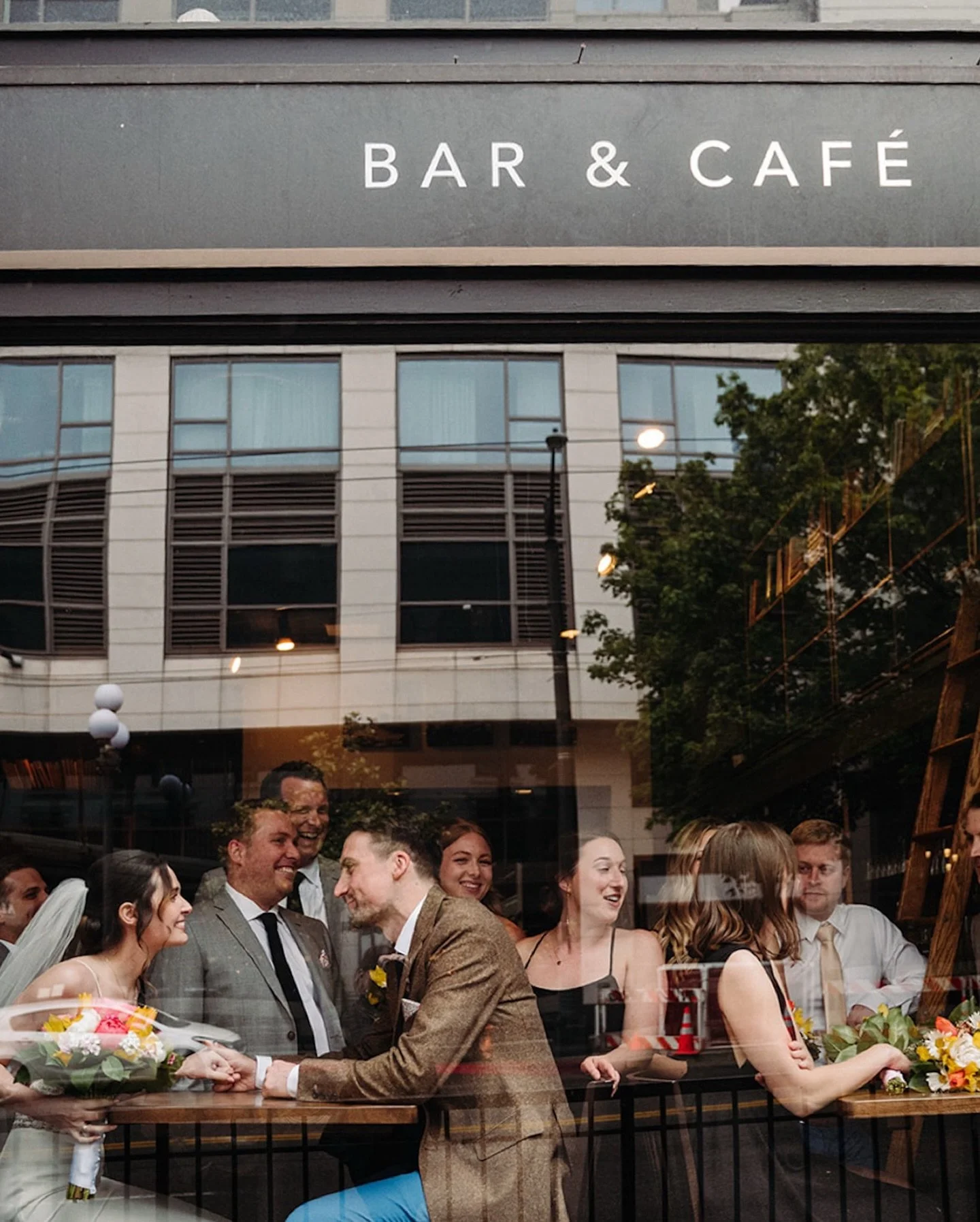 outside the bar before the ceremony in pioneer square seattle, the drinks flowing, wedding party chatting, and these two completely locked in on each other. scroll the carousel to see them stealing a kiss in the middle of the crowd like no one else e