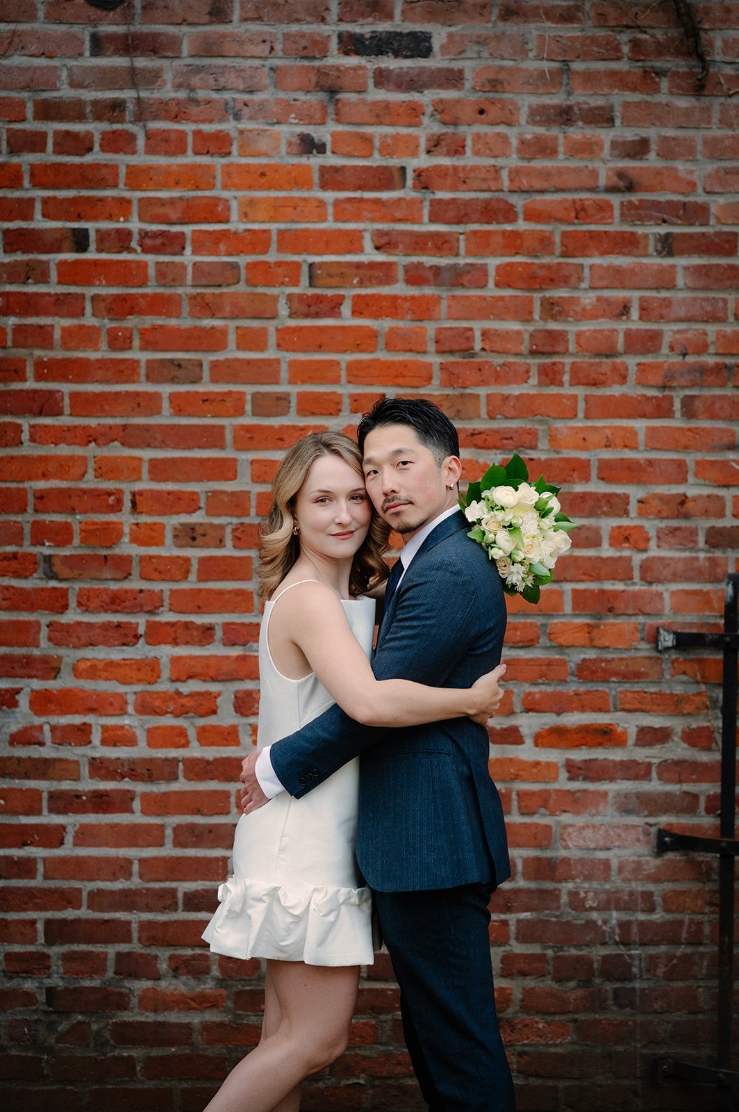elopement couple hugging in front of a red brick wall during their seattle elopement