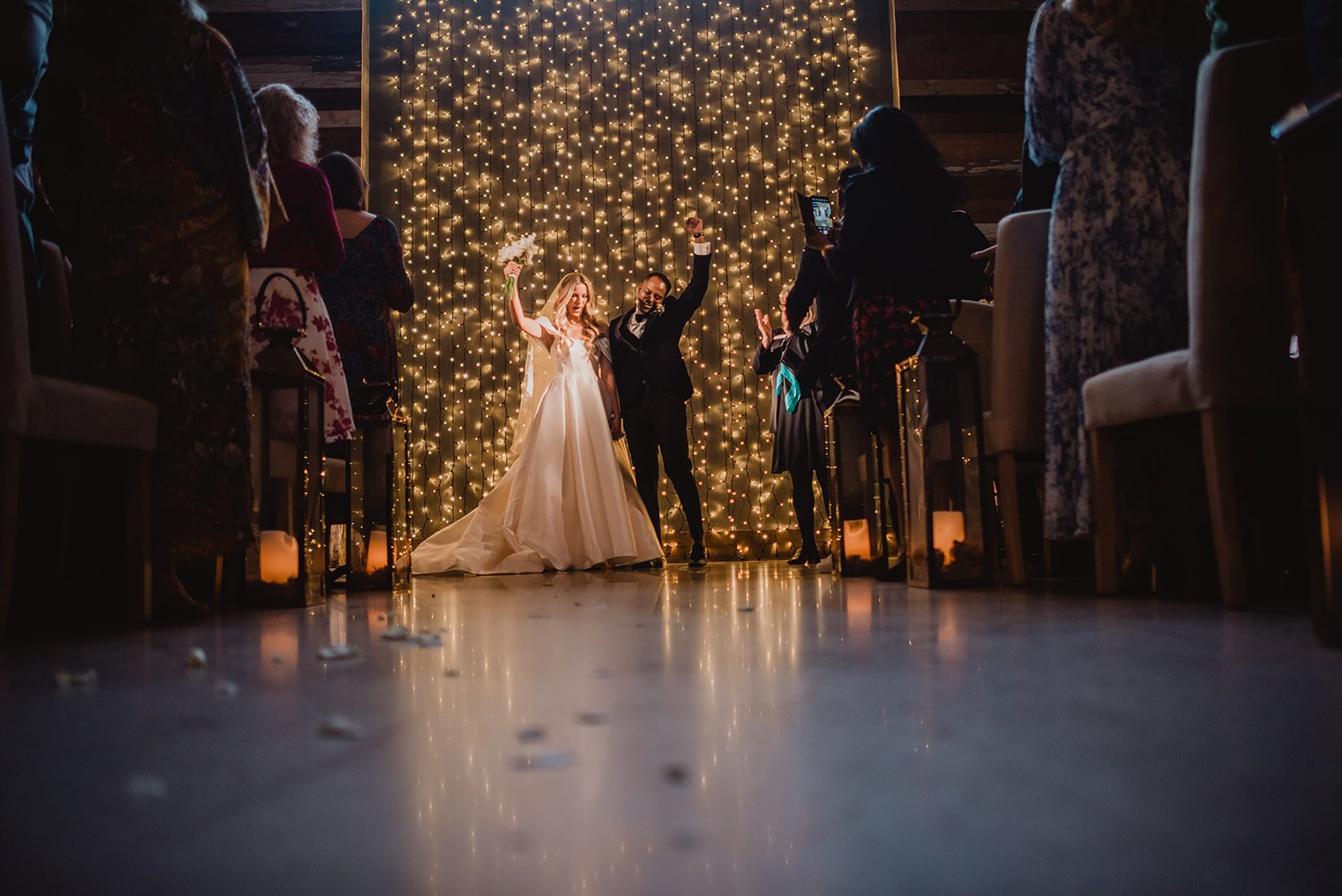 Bride and groom exiting the ceremony with a fairy light wall behind them