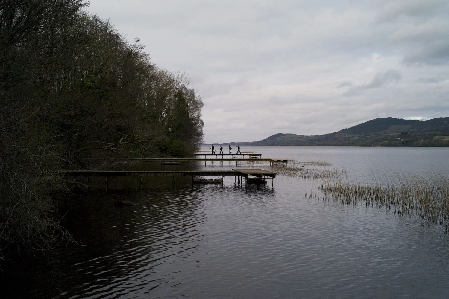 A documentary photograph of people walking on the dock of a lake in the west of ireland