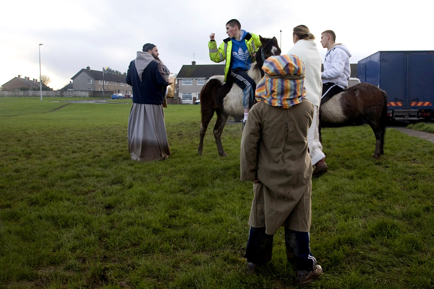 A documentary photograph of a boy watching a teenager on a horse yell at monk who is working in Moyross, Limerick, Ireland