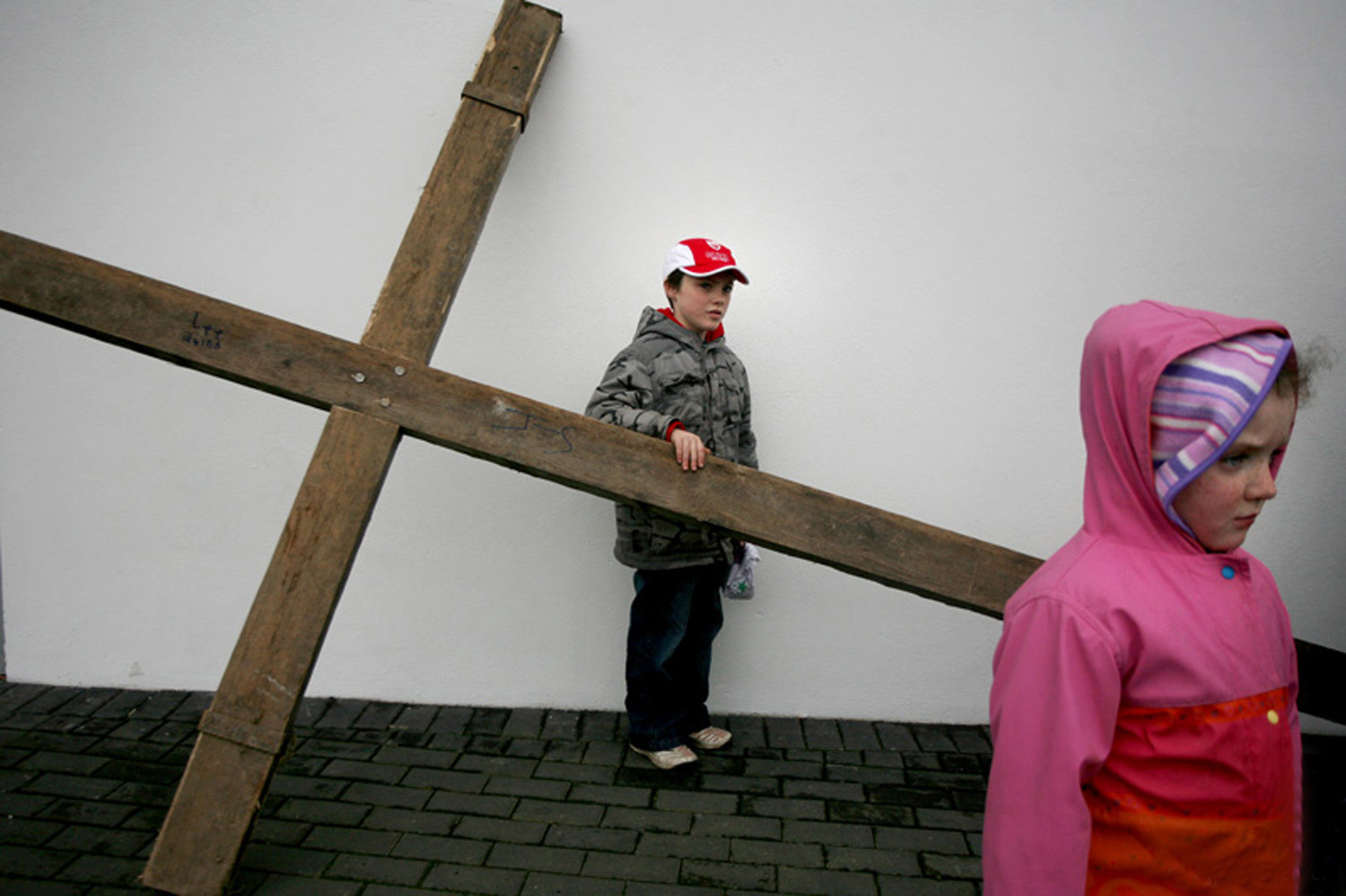 A documentary photograph of two kids standing by a large crucifix before the monks of Moyross perform the passion of the christ in Limerick, Ireland