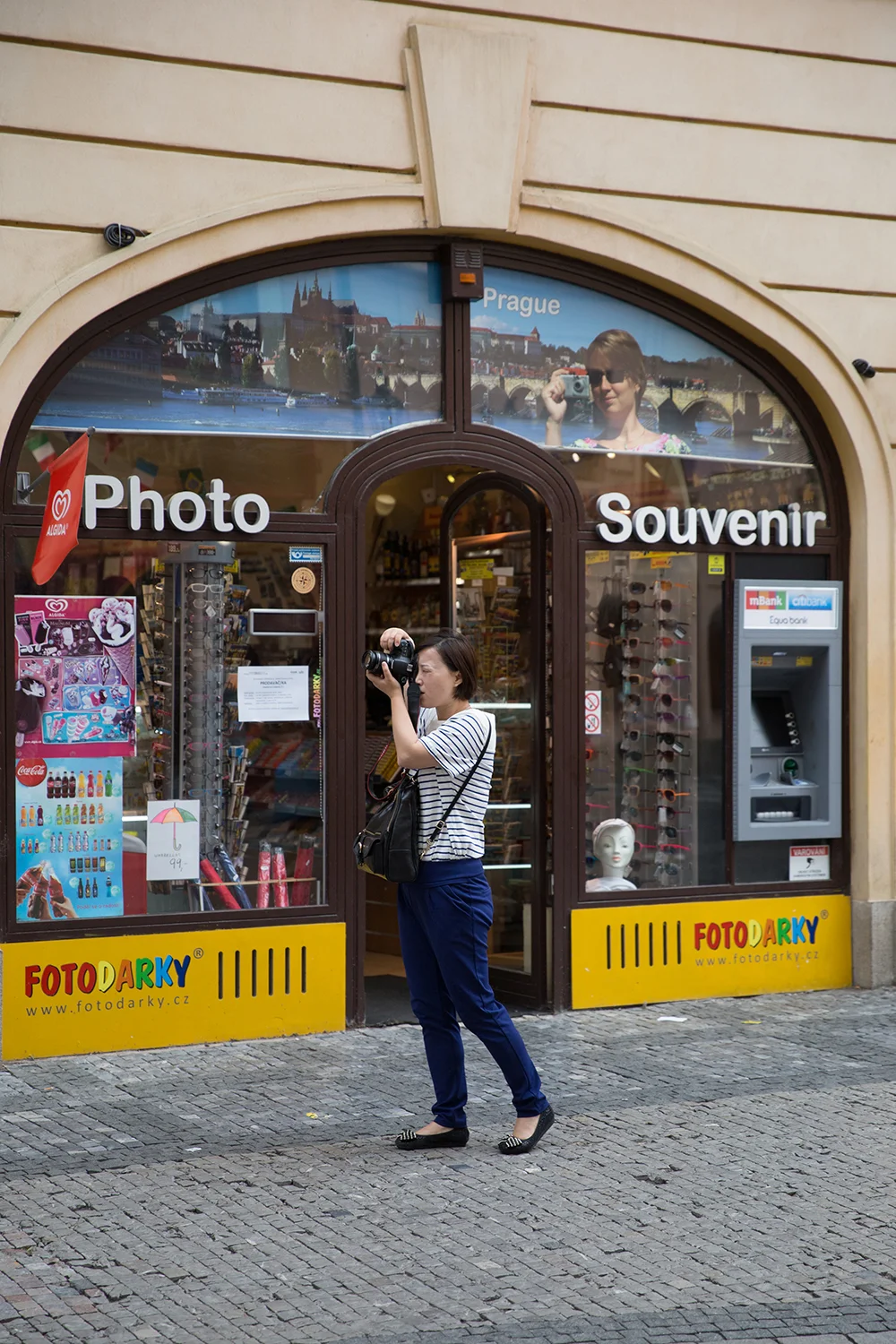 A documentary photograph of a tourist taking a photograph outside a photo and souvenir shop in Prague, Czech Republic