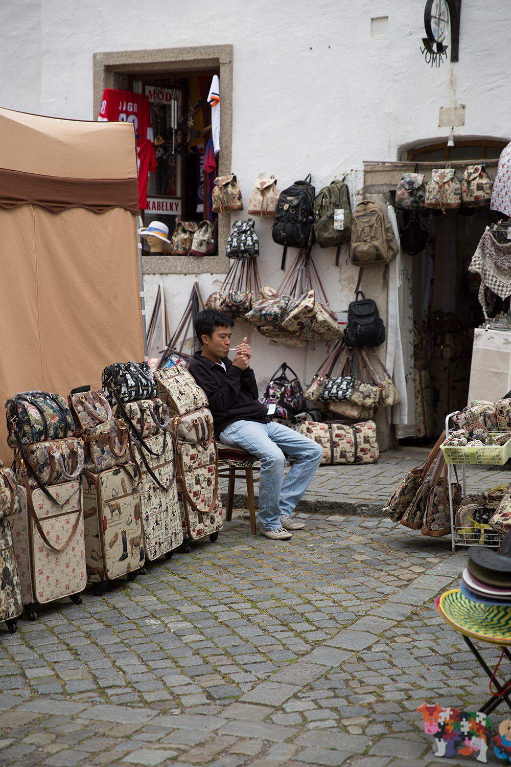 A documentary photograph of a shop owner smoking a cigarette outside his shop in Cesky Krumlov, Czech Republic during a festival