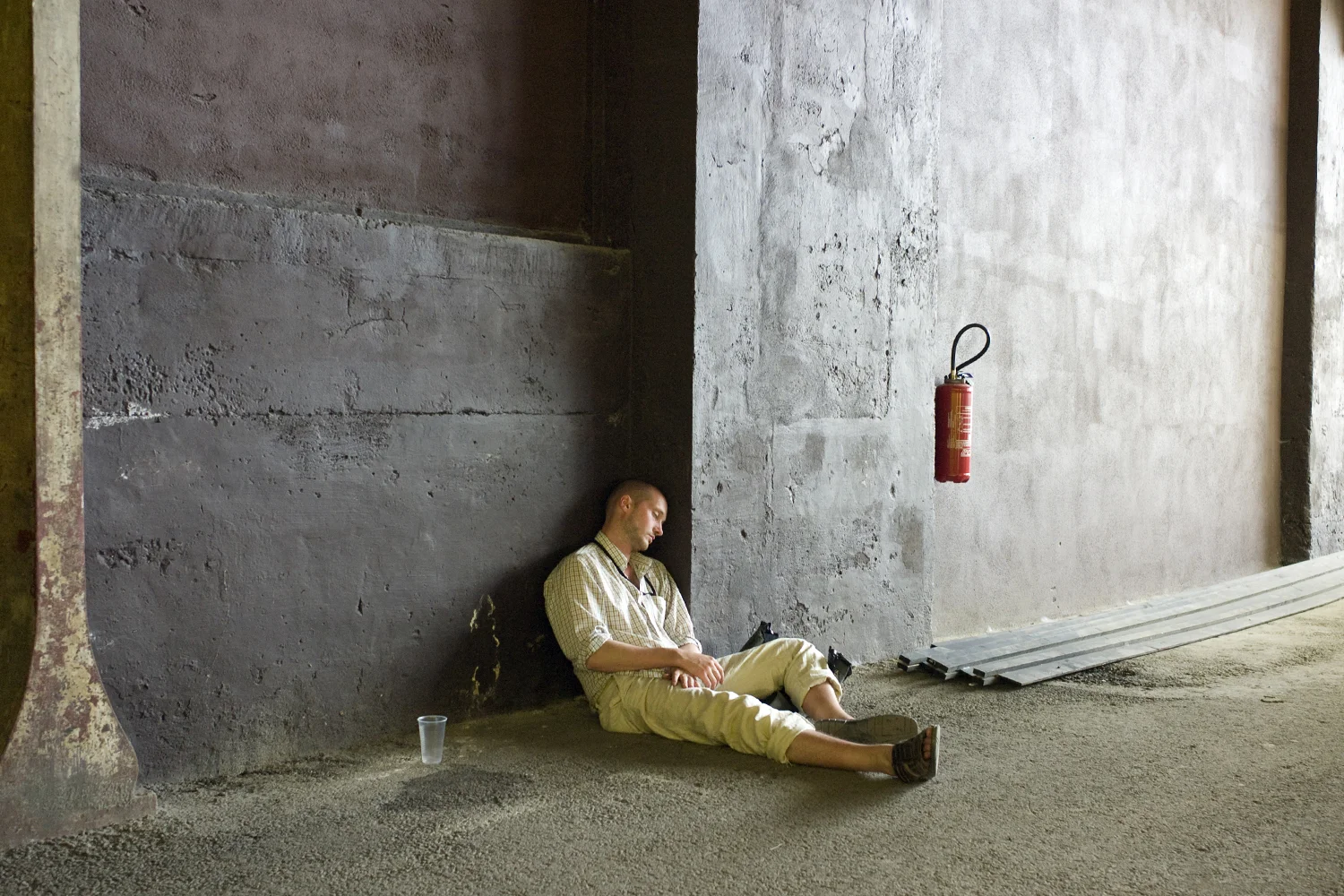 A documentary photograph of a man sleeping against the wall of an warehouse building in europe