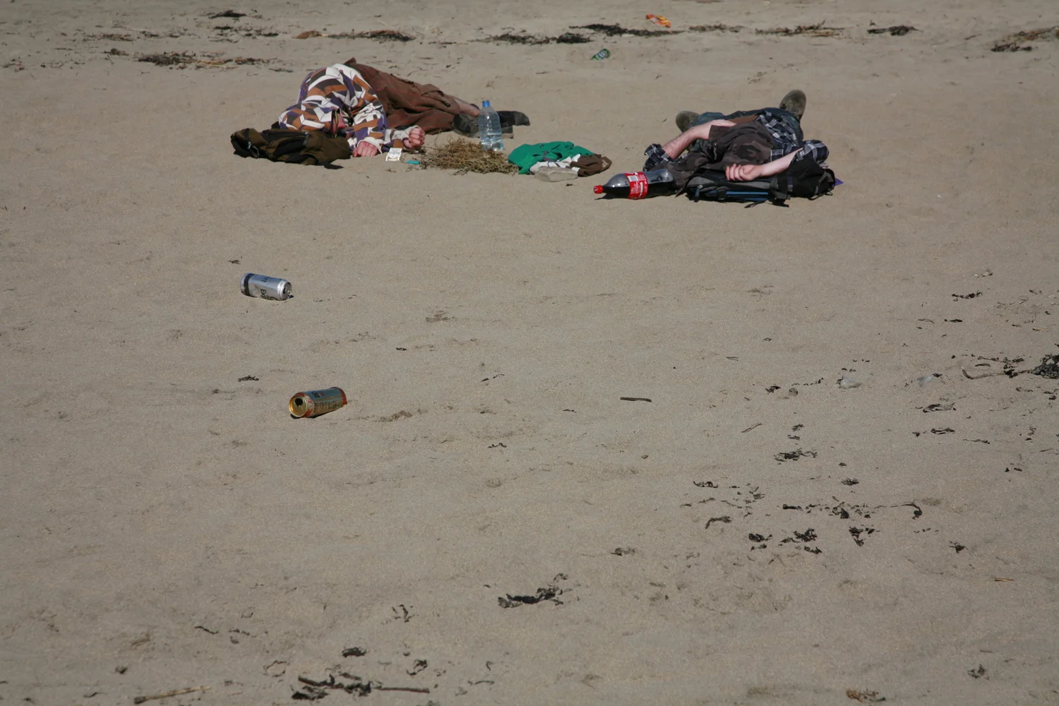 A documentary photograph of two hung over men laying on an irish beach with empty cans around them
