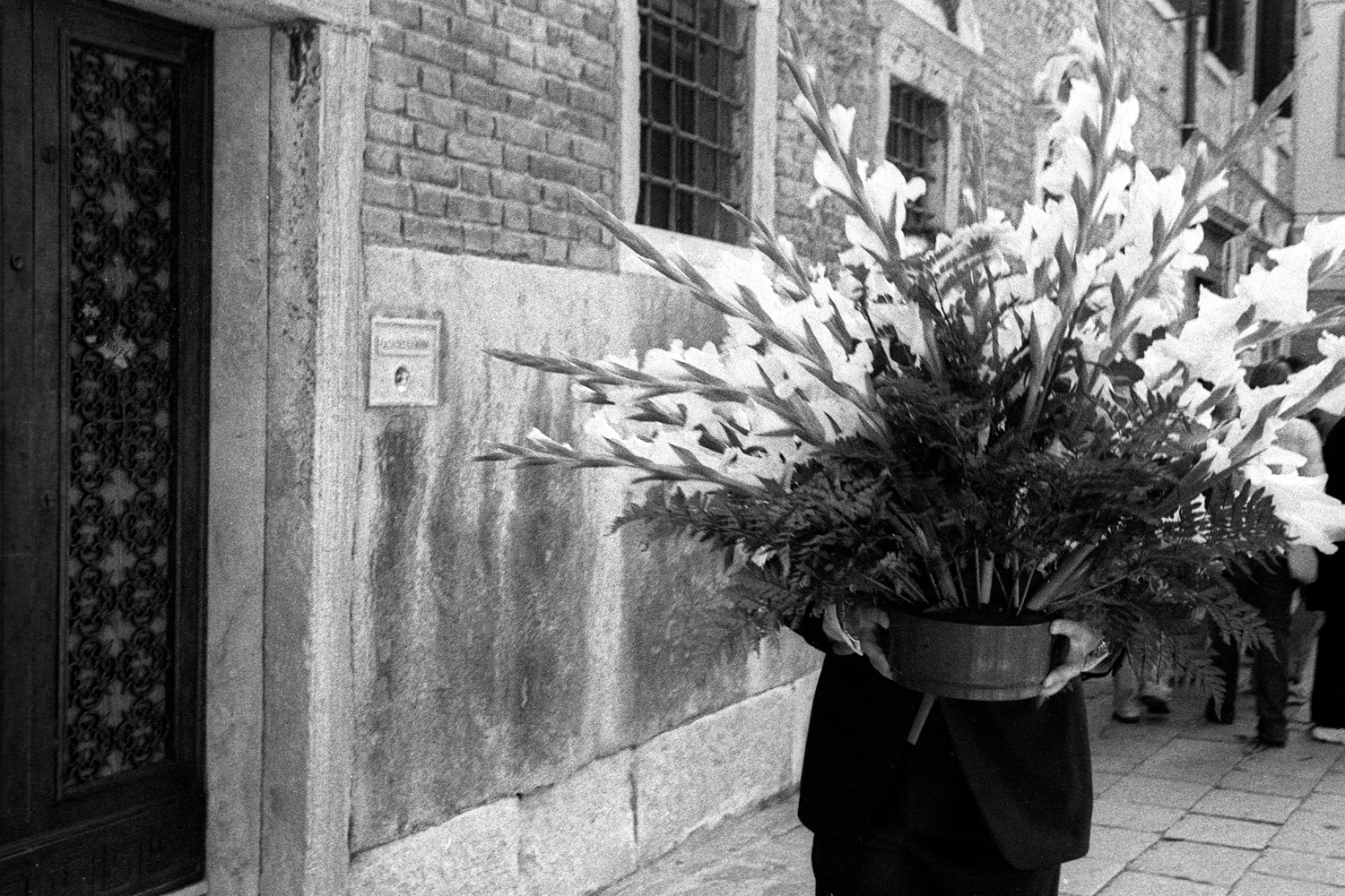 A documentary photograph of a person walking with flowers through the street of italy