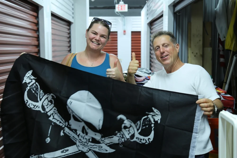 Summer Sarmiento poses with the pirate flag she bought from Frank Romanowski (right). For years, Frank has been homeless and selling a wide variety of flags on the streets of Miami.