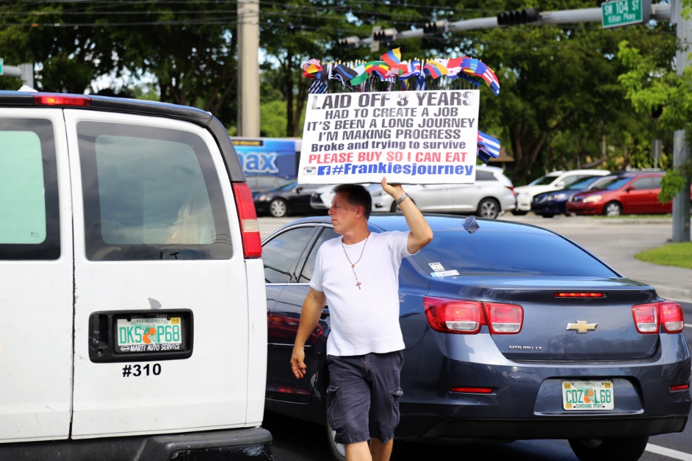 Frank walks between lanes of traffic while cars are stopped at a red light.