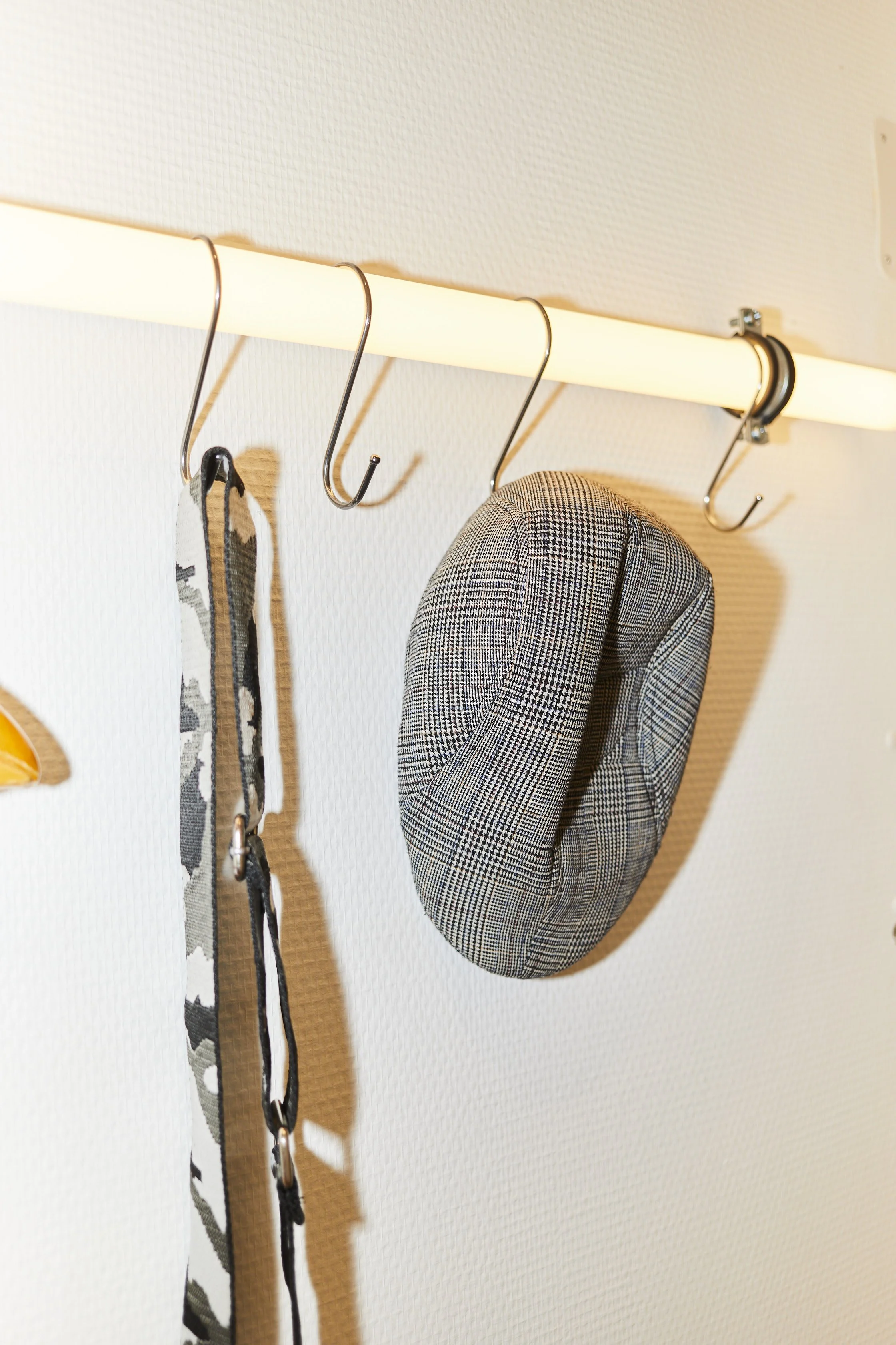 Crochets métalliques fixés à un plafond, avec un chapeau en tissu à carreaux suspendu et des bandes en tissu suspendues à un crochet.